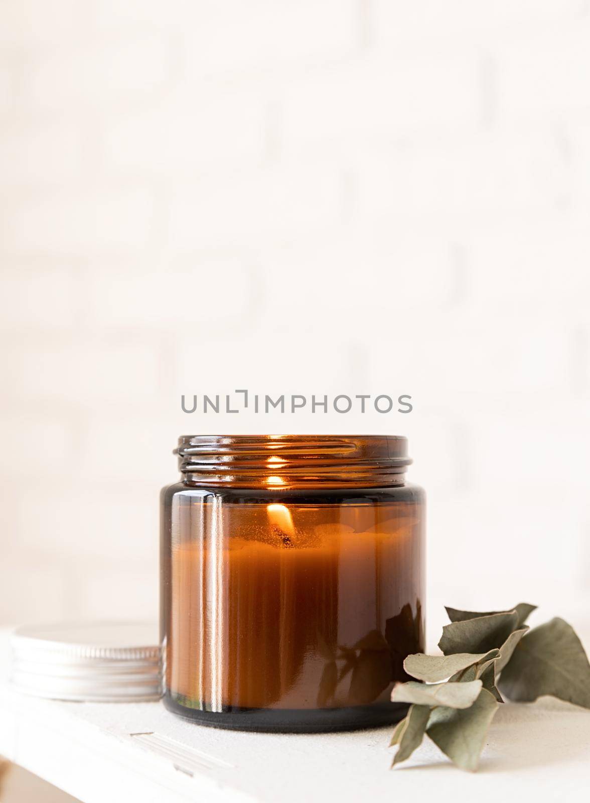 Home decoration and interior. Beautiful burning candle with eucalyptus leaves on white brick wall background