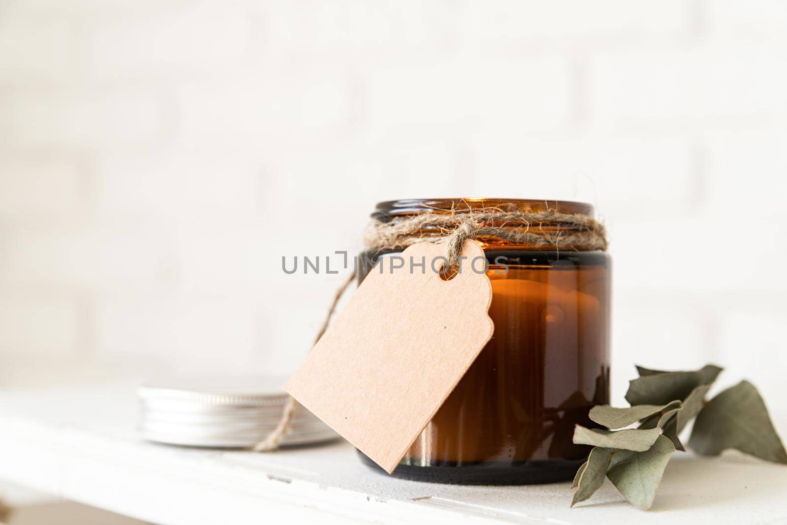 Home decoration and interior. Beautiful burning candle with eucalyptus leaves on white brick wall background