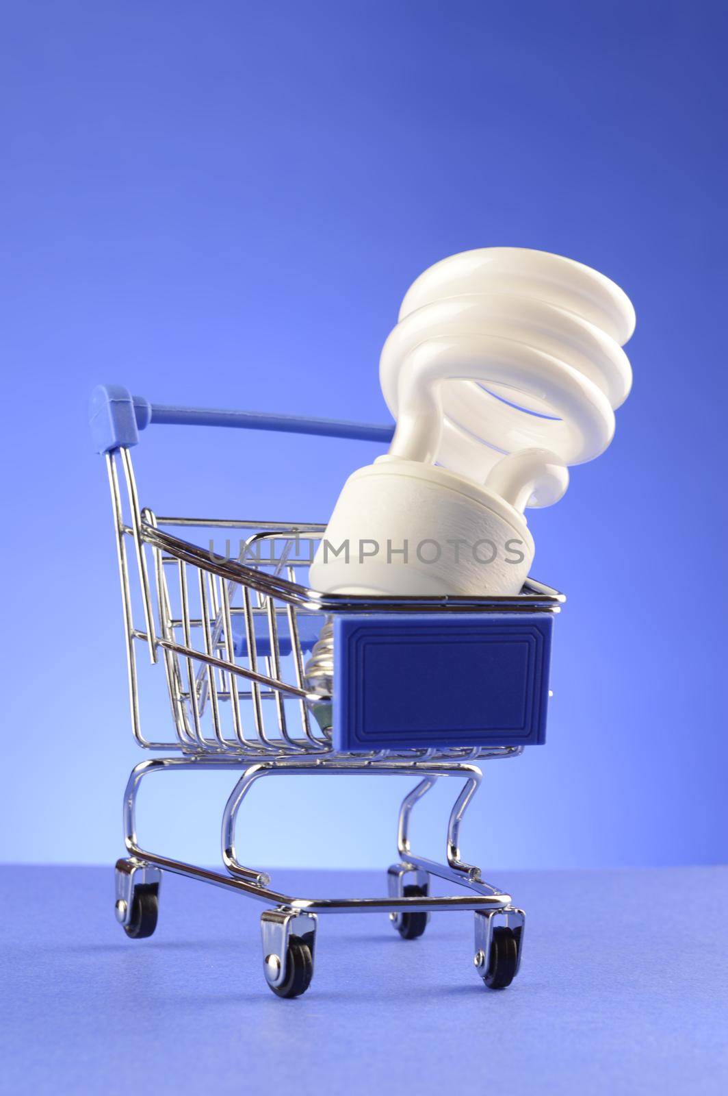 A CFL bulb is inside a miniature shopping cart over a blue background.