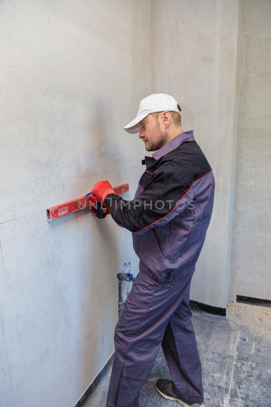 A man, an electrician marks out with a pencil, tape measure and a linear level for drilling holes for sockets