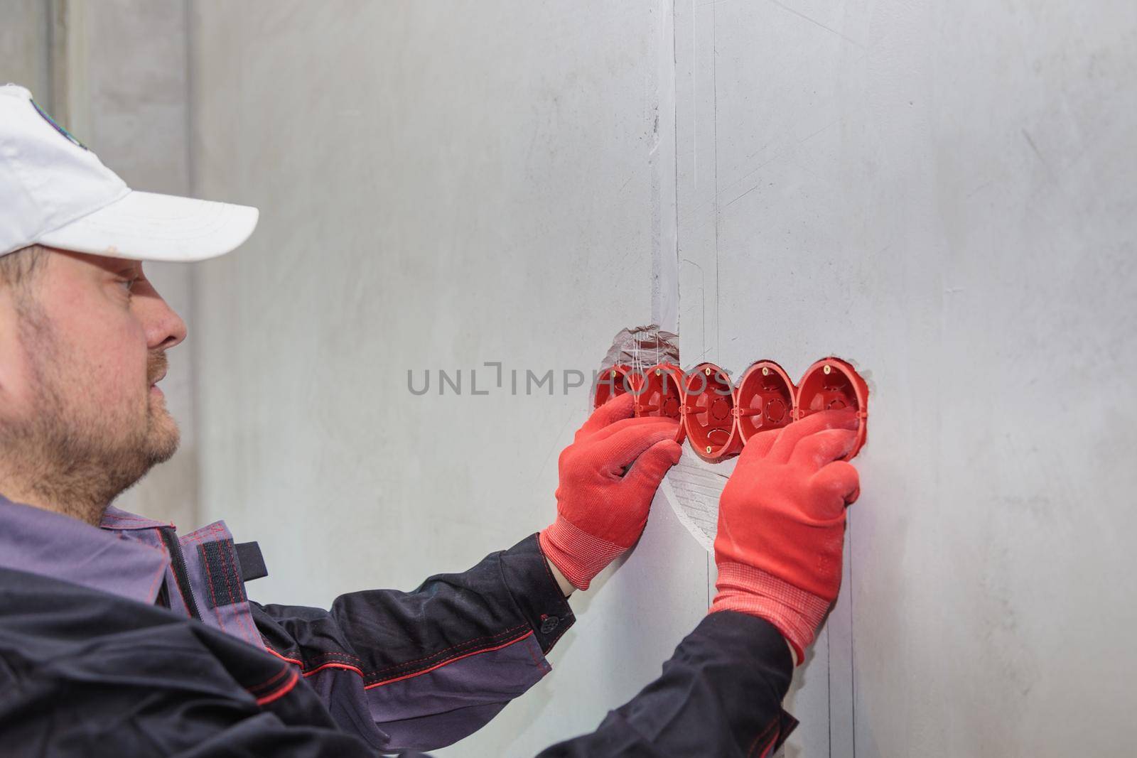 The electrician inserts the plastic box directly into the outlet holes. Close-up