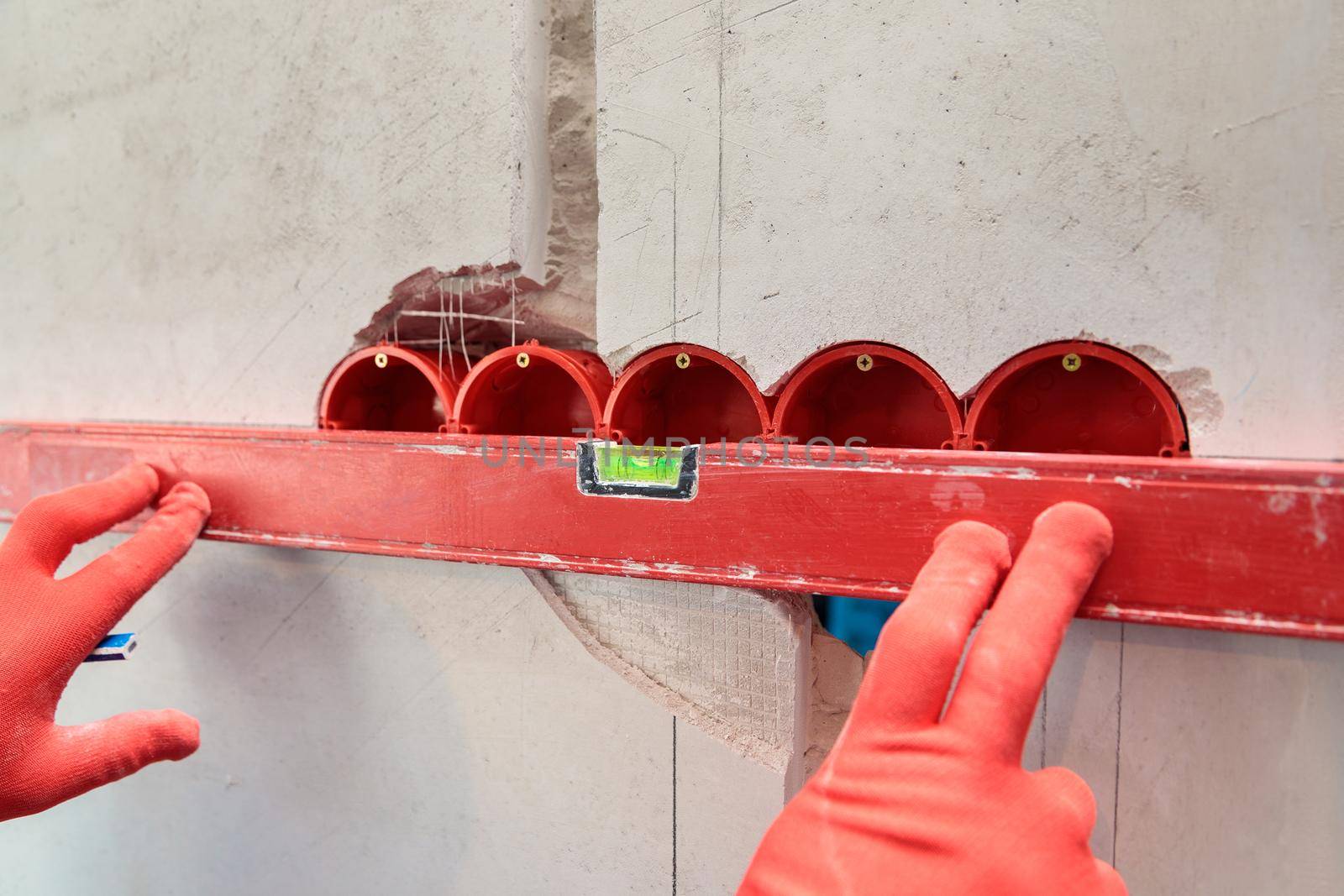 A man, an electrician marks out with a pencil, tape measure and a linear level for drilling holes for sockets