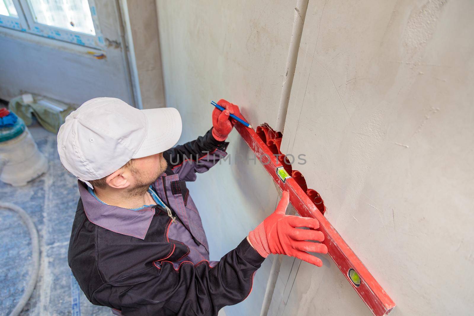 A man, an electrician marks out with a pencil, tape measure and a linear level for drilling holes for sockets