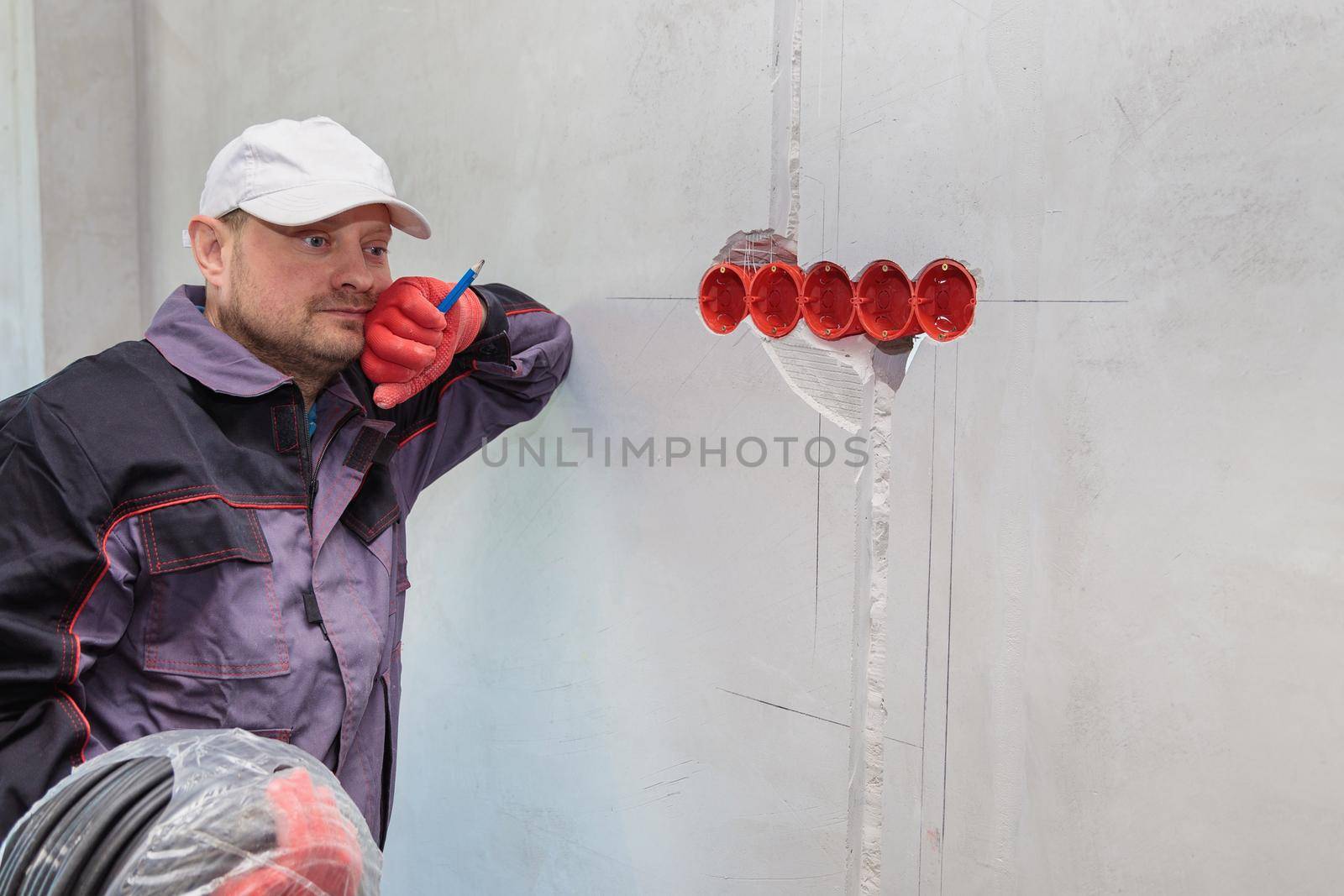 An electrician stands against the wall with an electrical cable for sockets. Close-up