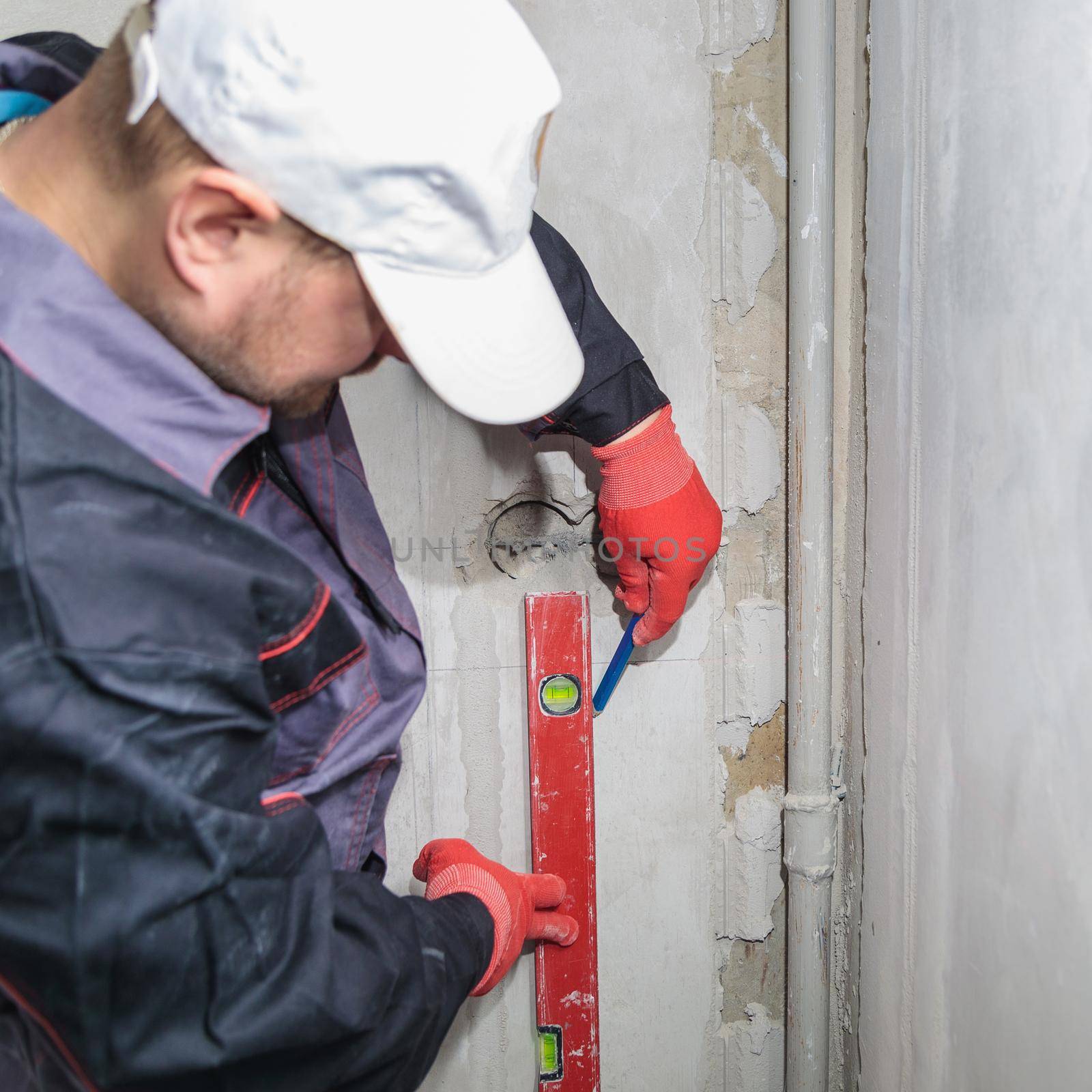 A man, an electrician marks out with a pencil, tape measure and a linear level for drilling holes for sockets