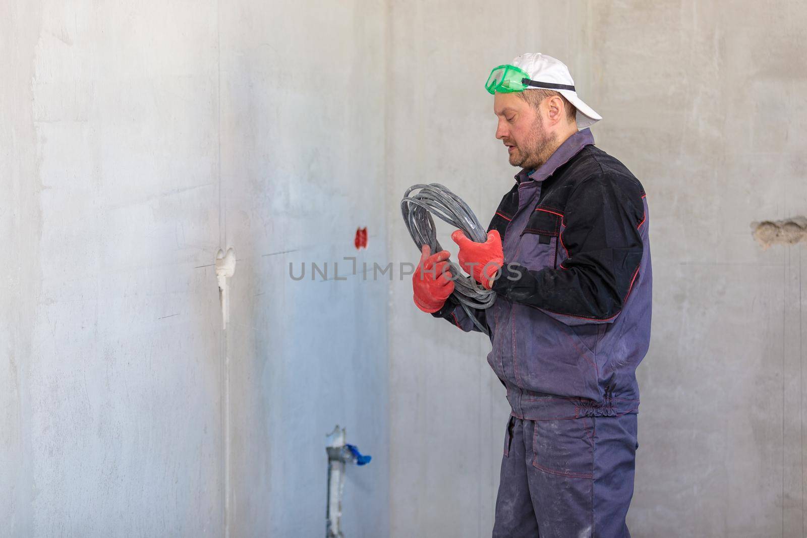 An electrician stands against the wall with an electrical cable for sockets. Close-up