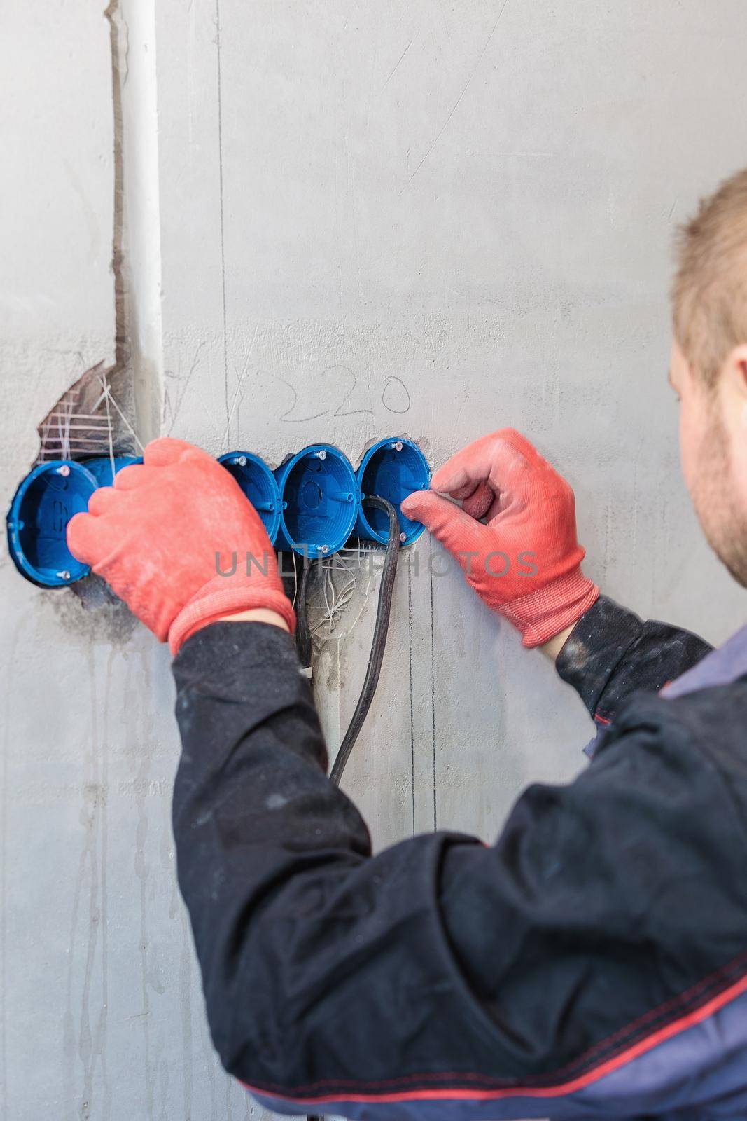 The electrician inserts the plastic box directly into the outlet holes. Close-up