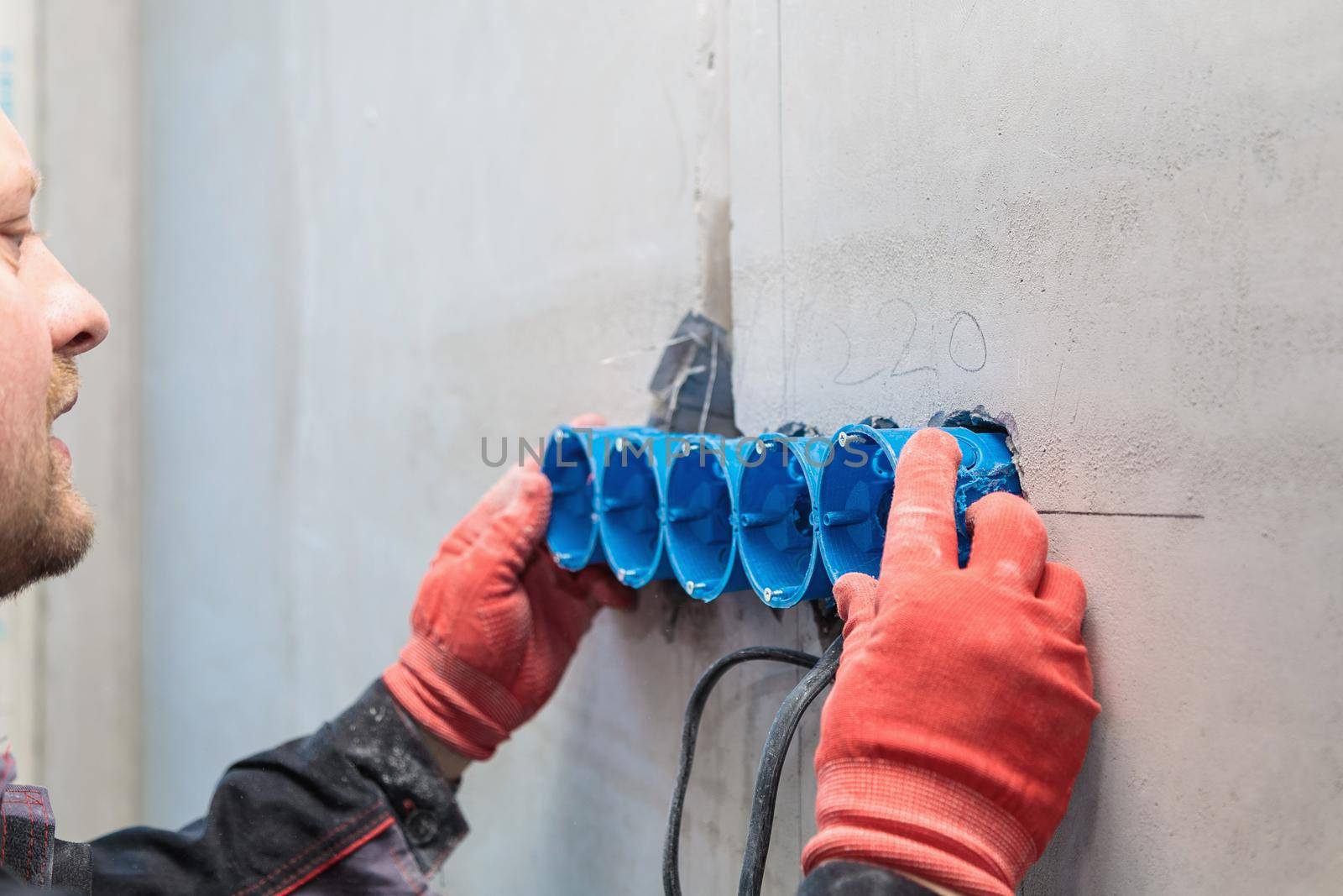 The electrician inserts the plastic box directly into the outlet holes. Close-up