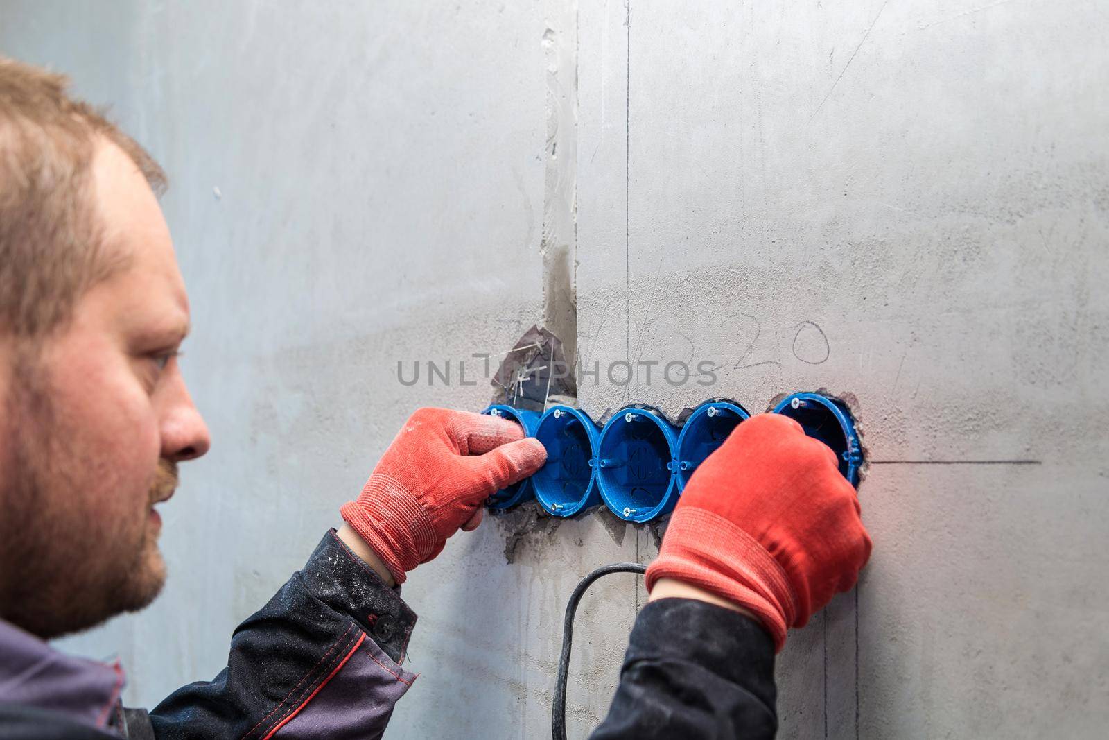 The electrician inserts the plastic box directly into the outlet holes. Close-up
