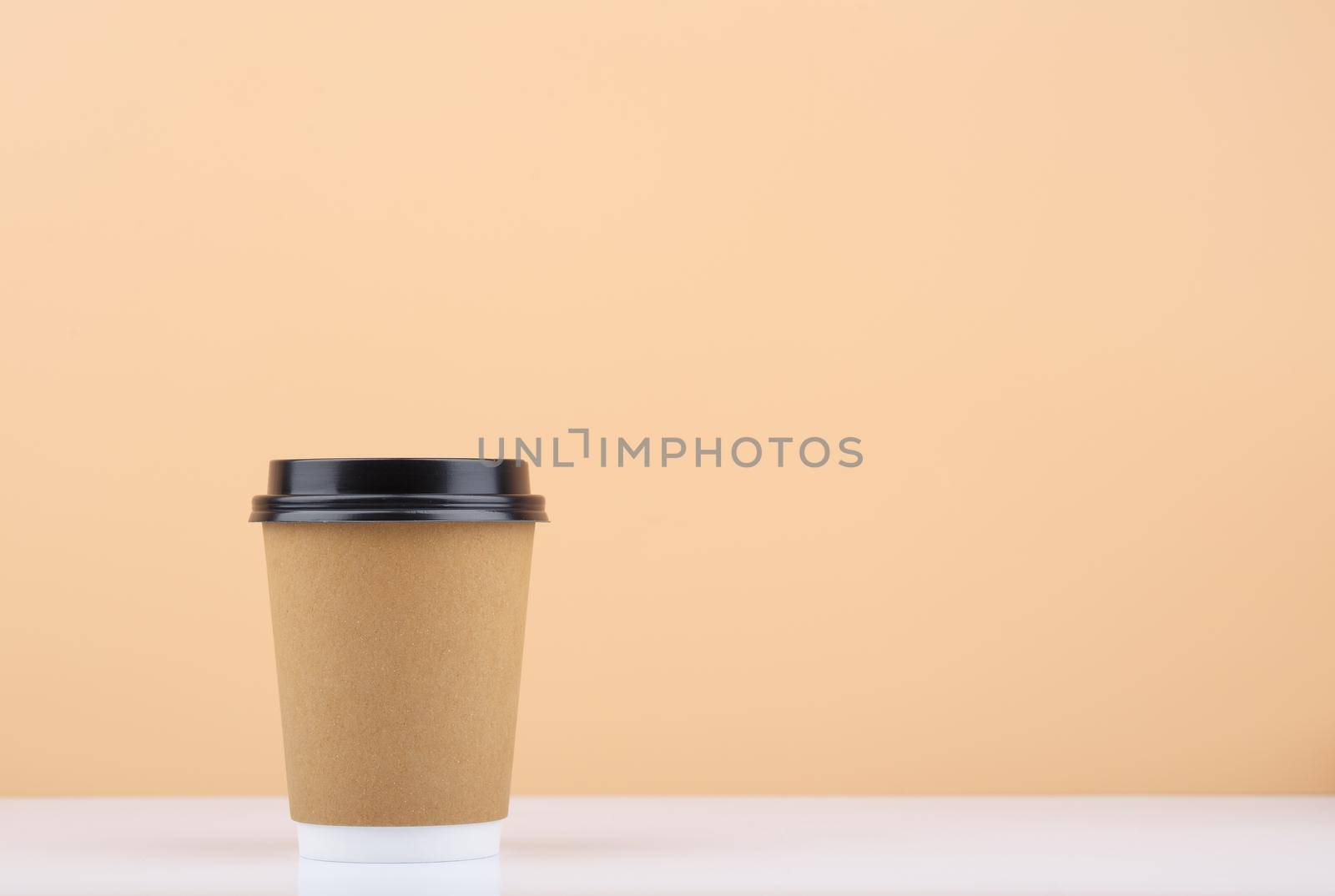 Disposable coffee cup on white table against light beige background with copy space. High quality photo