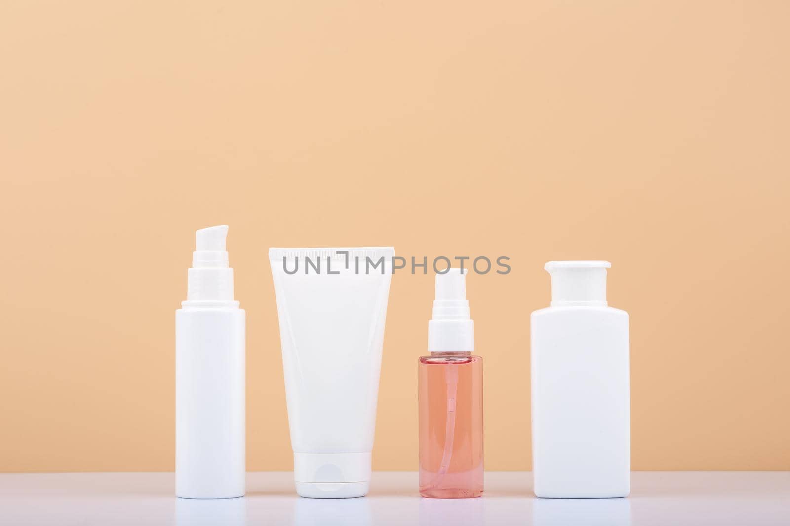 Skin care products in a row on white glossy table against beige background. Beauty and cosmetic concept. Minimalistic still life with beauty products