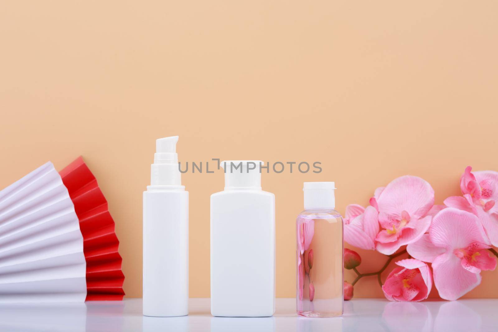 Face cream, cleaning foam and moisturizing or exfoliating lotion against beige background with wavers and flowers. Concept of organic skin care products and daily skin routine