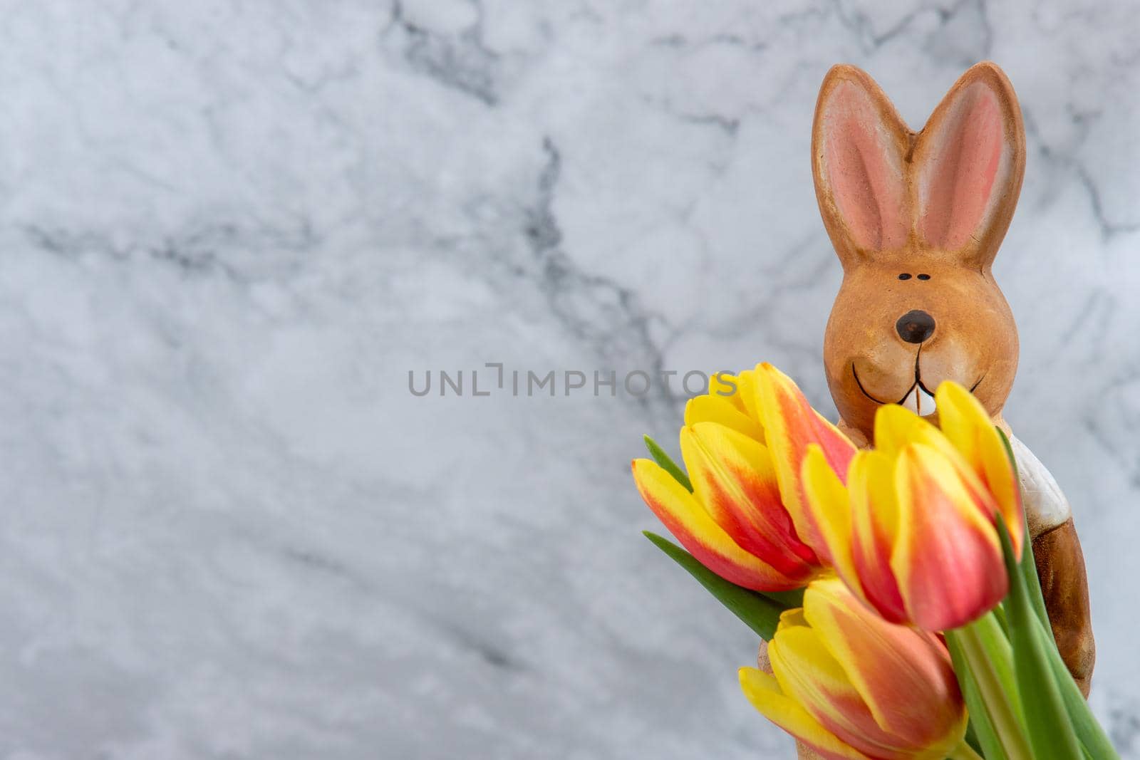 Porcelain easter bunny with yellow red tulip flowers against a grey marbled background