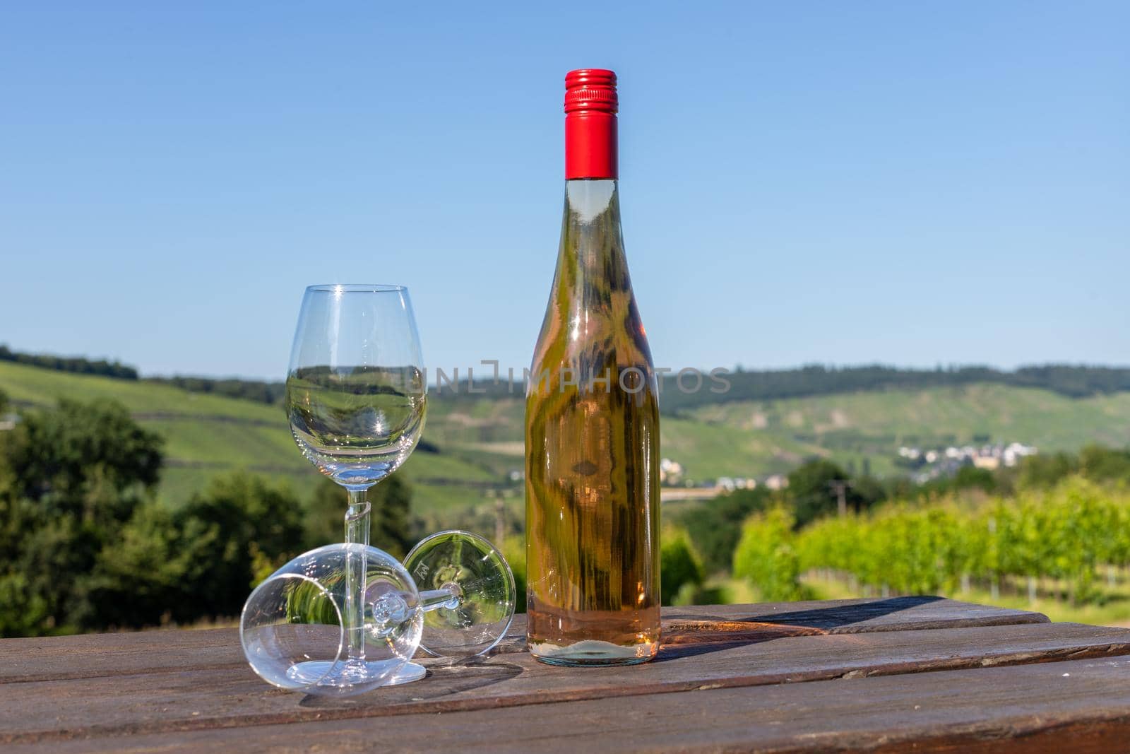 Wine bottle with glasses on wooden table with landscape on river moselle in background