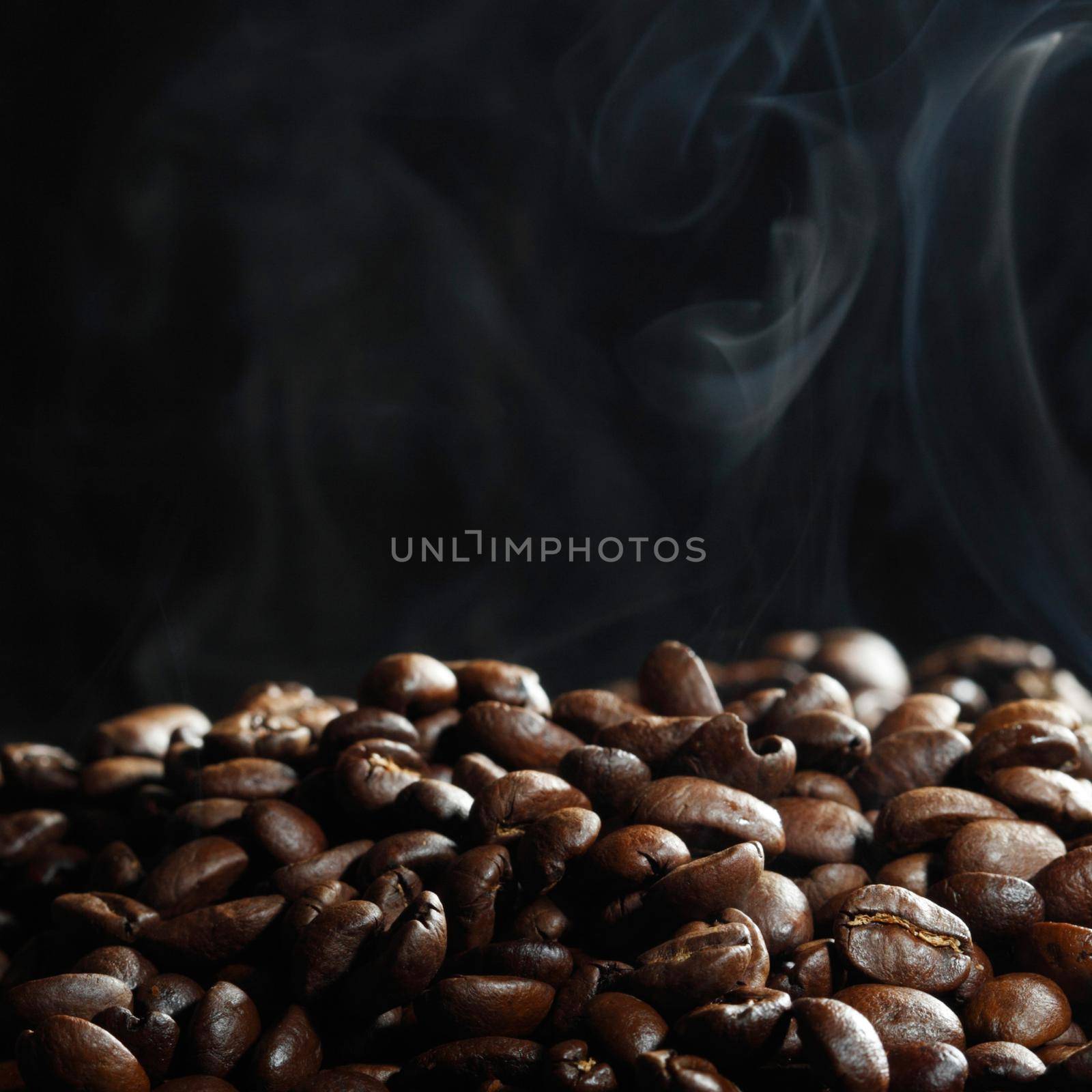 Hot roasted coffee beans and steam on black background with copy space