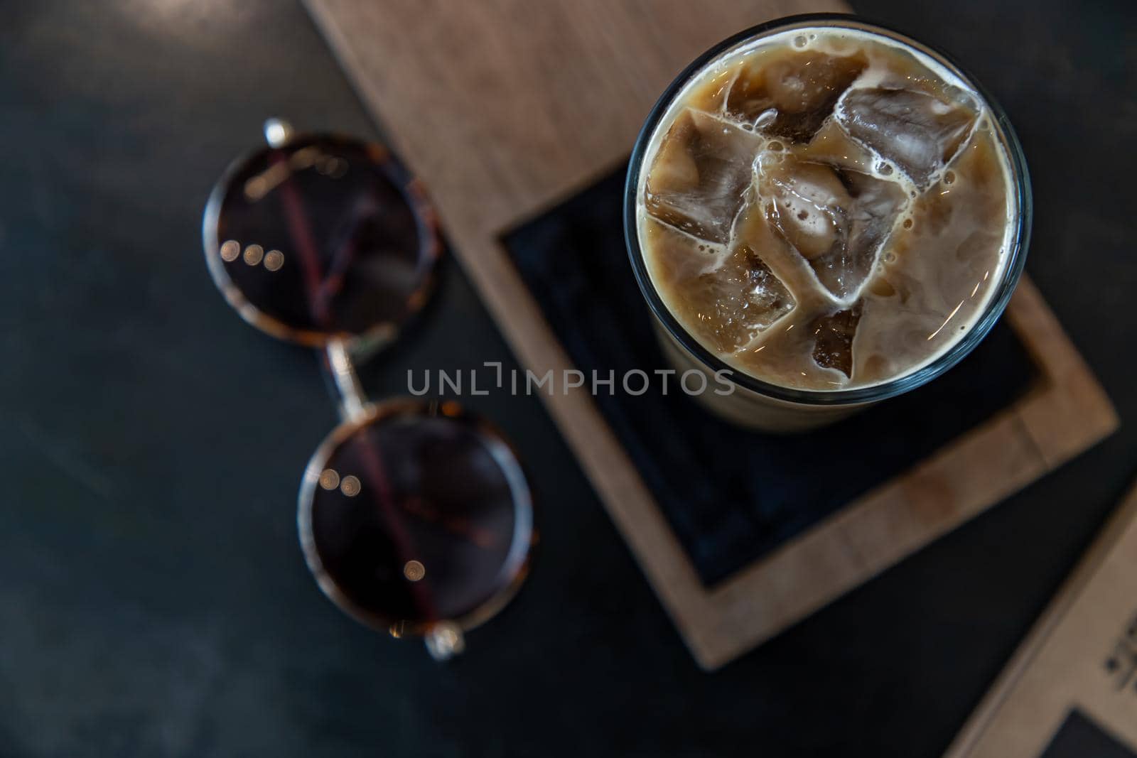 Cold coffee in a tall glass with ice cubes on wooden background. Cold summer drink on a black background with copy space. Focus and blur.