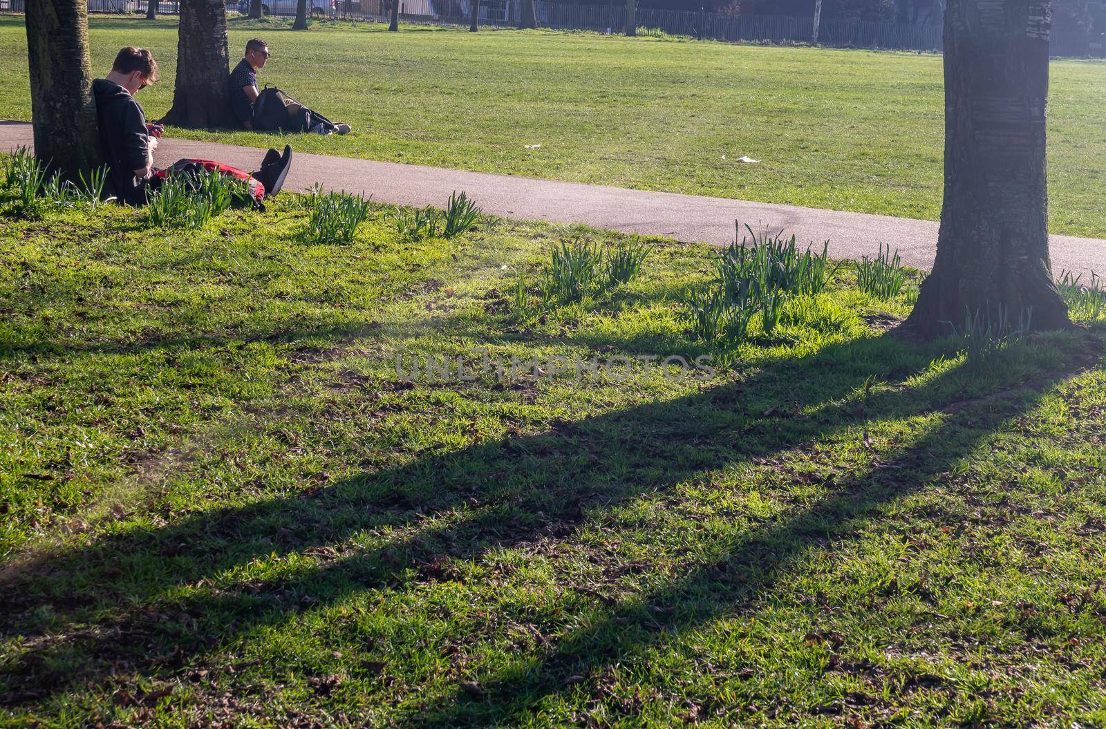 London, United Kingdom - Feb 24, 2019 : Two young mans  sit and relax on a green lawn in a park. Summer afternoon in the park. No focus, specifically.