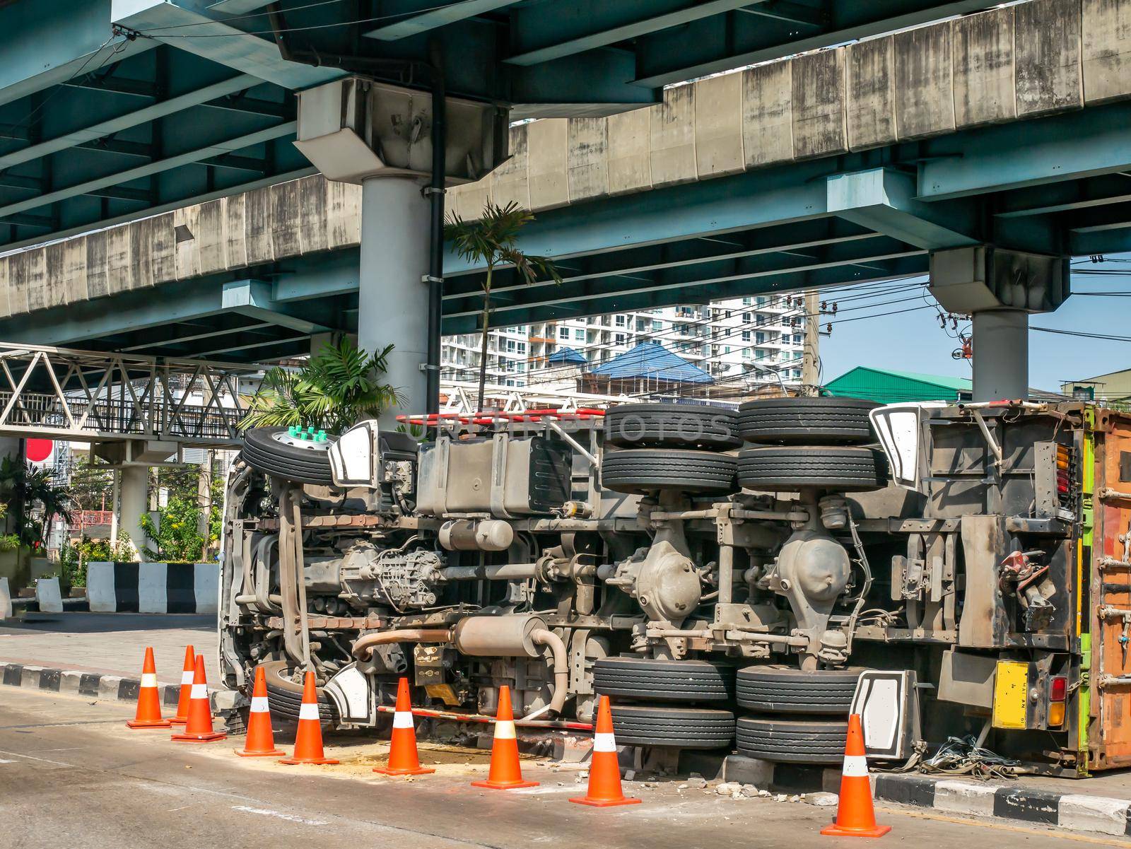 A view of under the truck carrying a container overturned on a road under a bridge over an intersection.