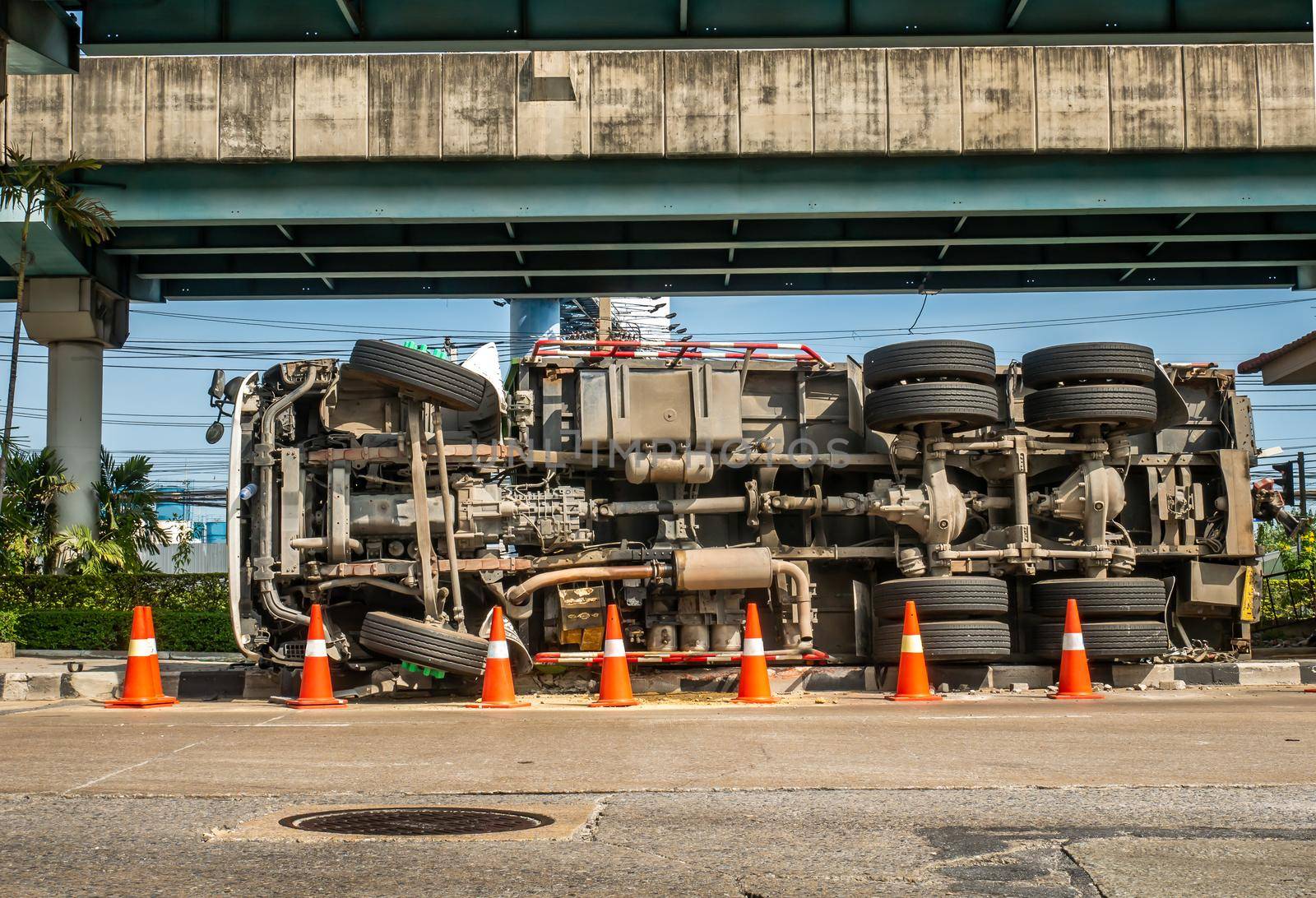 A view of under the truck carrying a container overturned on a road under a bridge over an intersection.
