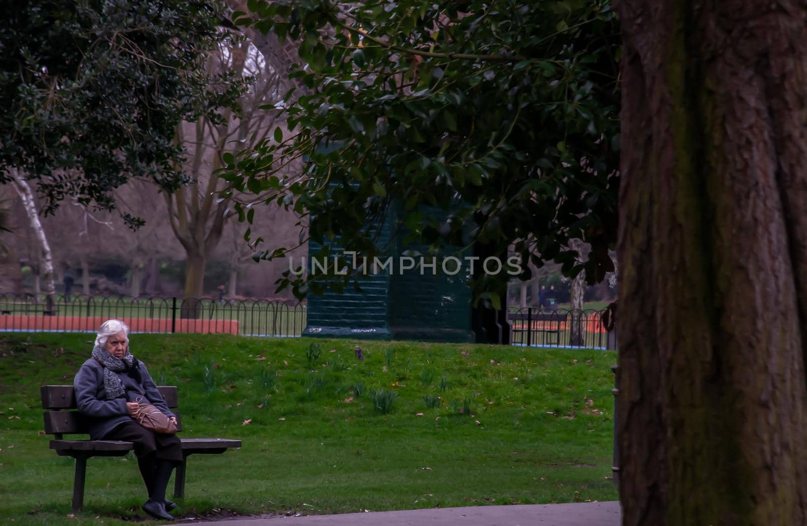 London, United Kingdom - APR 12, 2019 : Elderly caucasian woman sitting on wooden chair in park bench. No focus, specifically.