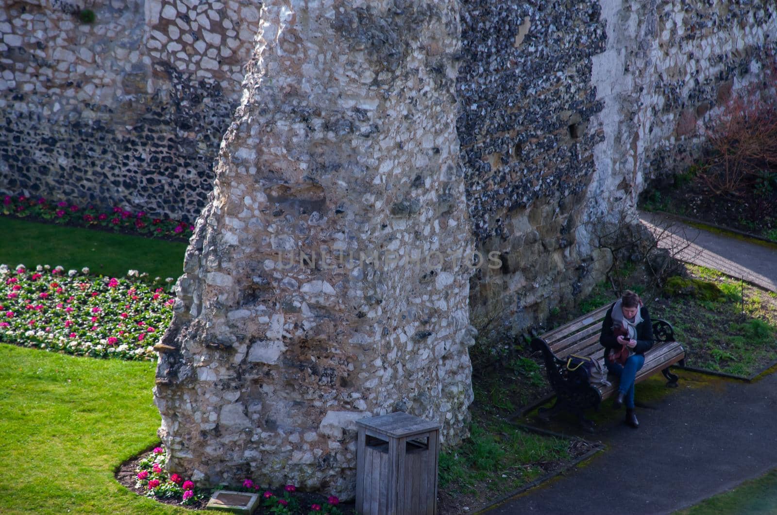 Guildford, United Kingdom - May 05, 2019 : A woman sit and pressing mobile on wooden bench in Guildford Castle and Grounds. No focus, specifically.