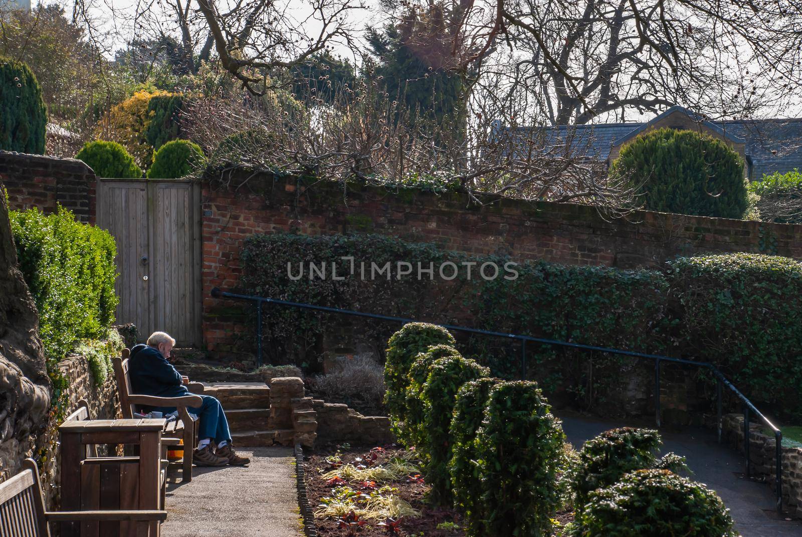 Guildford, United Kingdom - May 05, 2019 : Elderly man relaxing on wooden bench in park. No focus, specifically.