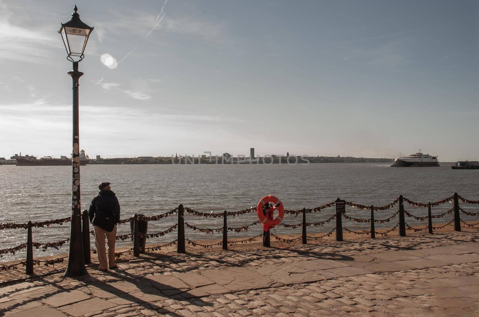 Liverpool, United Kingdom - 03 Jan 2019 : The back of Lonely young man standing under the Street lamp on the river walk and looking at skyline. No focus, specifically.