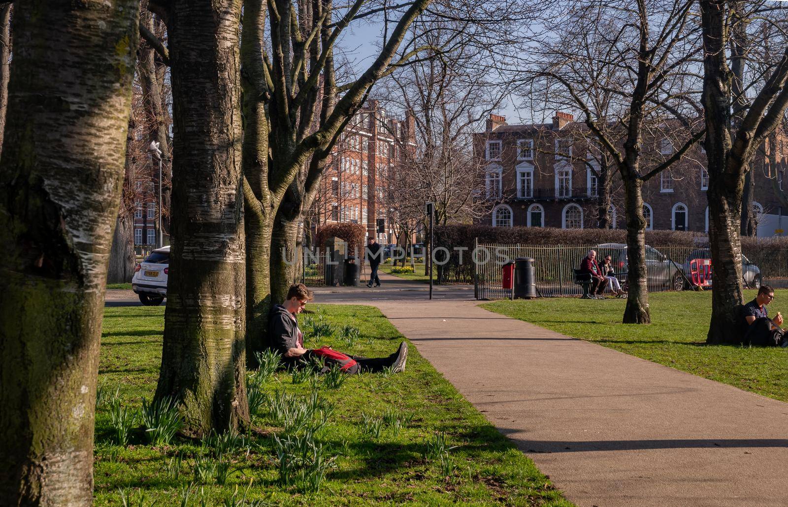 London, United Kingdom - Feb 24, 2019 : People sit and relax on a green lawn in a park. Summer afternoon in the park. No focus, specifically.