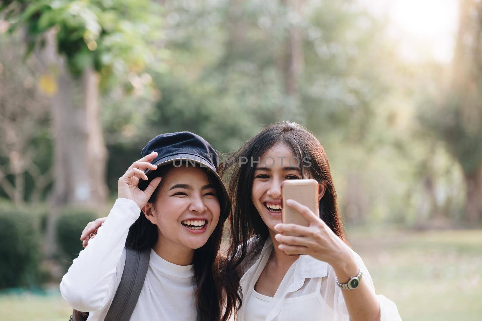 Happy two young attractive asian girls take a selfie at the park by nateemee