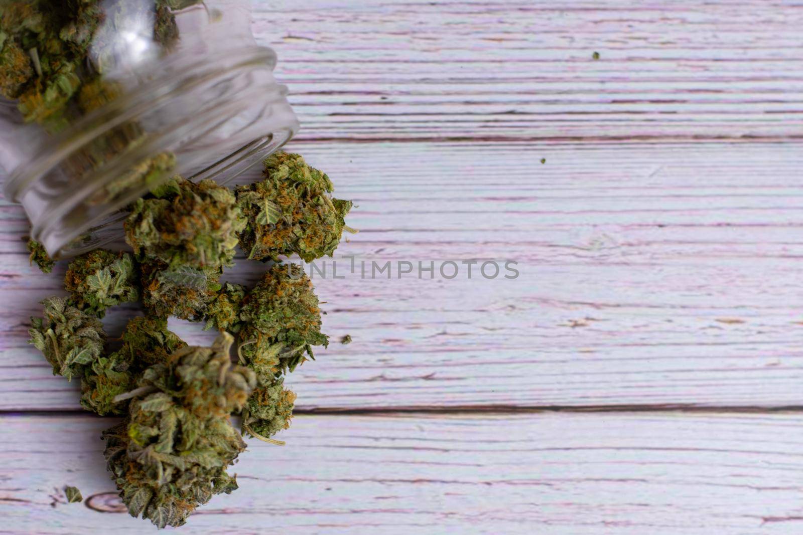 Looking down on a glass mason jar with orange and green cannabis nugs pouring out of it on a wood background