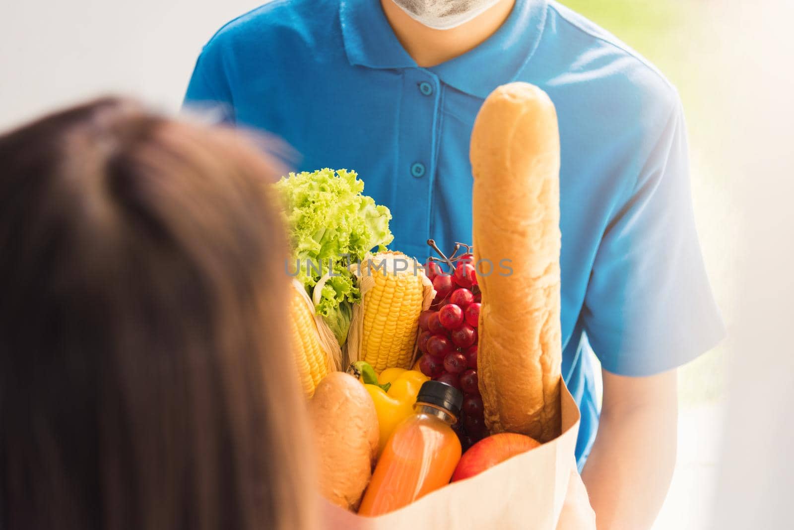 Asian young delivery man in uniform wear protective face mask he making grocery service giving fresh food to woman customer receiving front house under pandemic coronavirus, Back to new normal concept