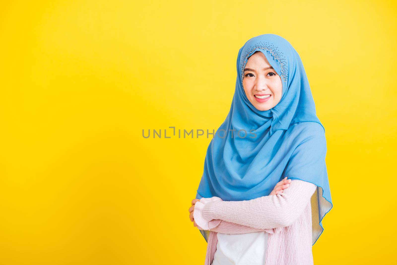 Asian Muslim Arab, Portrait of happy beautiful young woman Islamic religious wear veil hijab she smiling stand crossed arm, studio shot isolated on yellow background