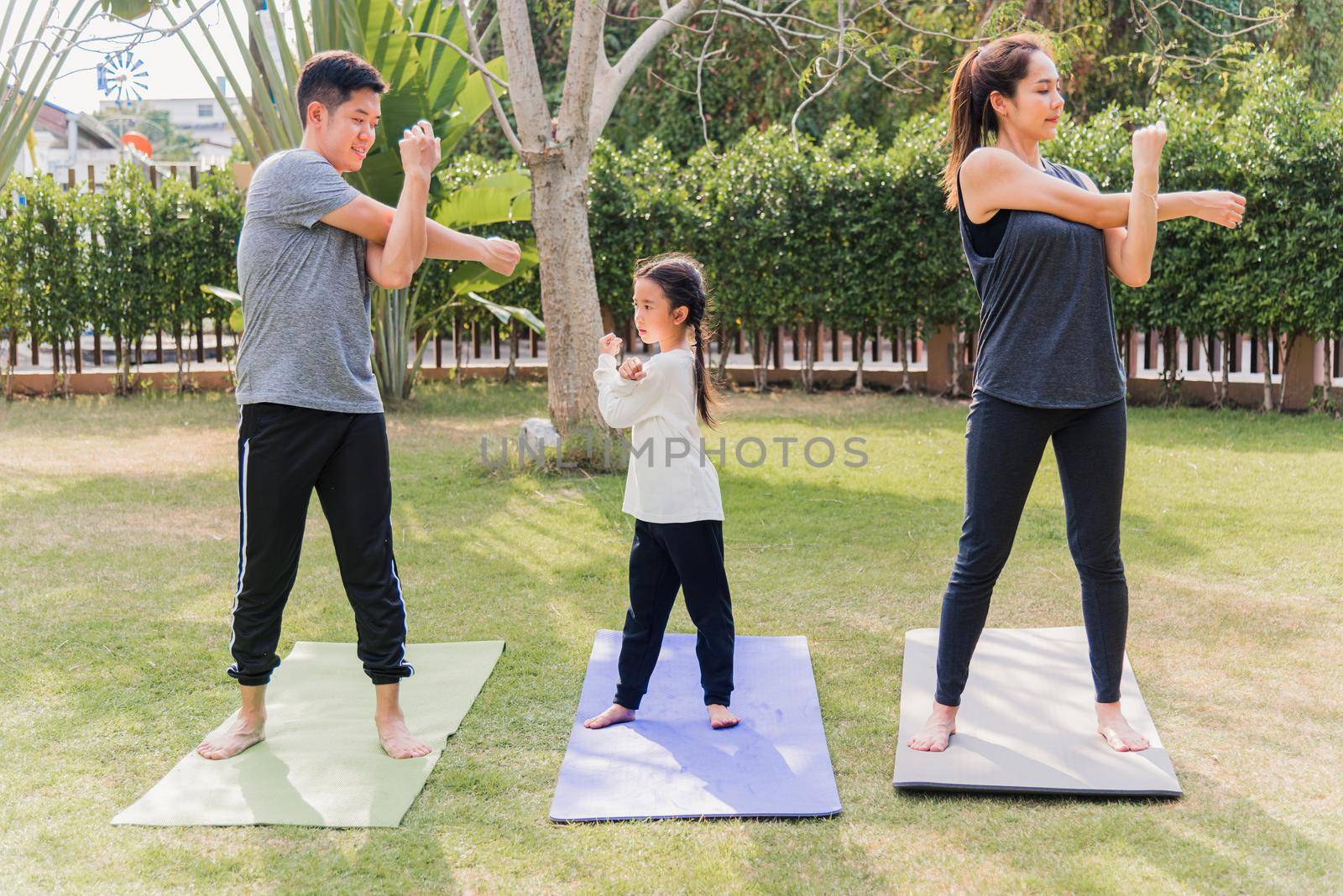 Asian young mother, father and child daughter practicing exercising stretching together before yoga workout outdoor morning in nature a field garden park. Happy family kid sport healthy lifestyle