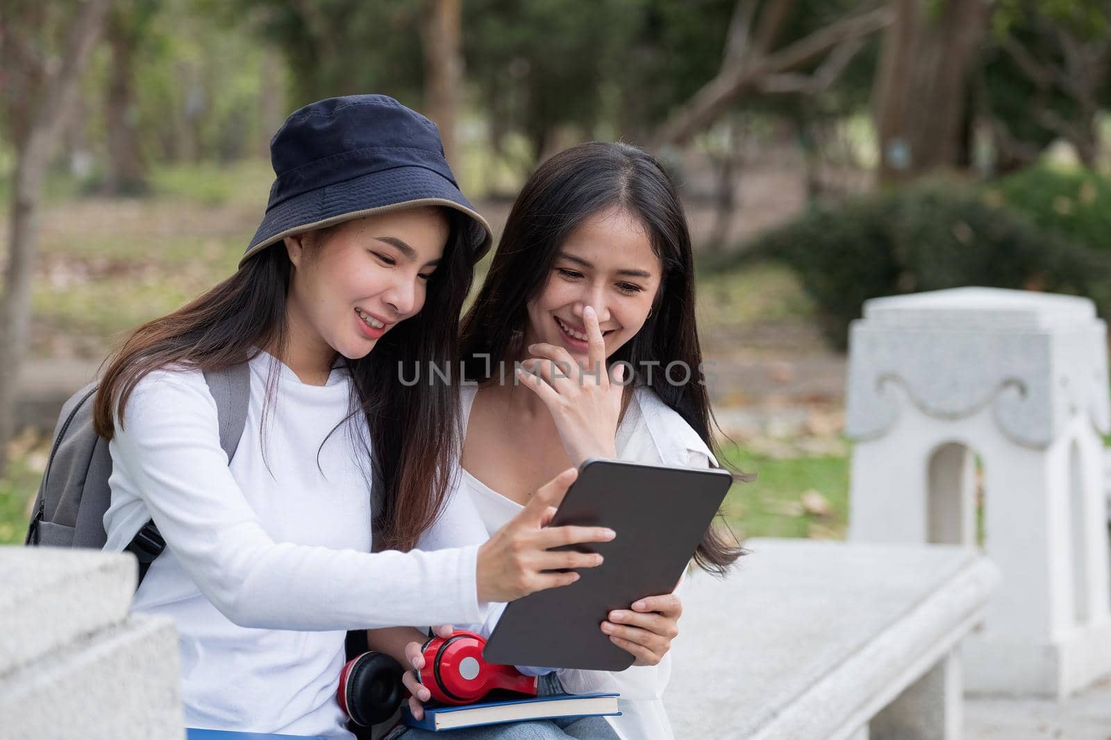 Asin female students wearing casual clothes sitting at outdoor having deep looks in books. Cute female explaining something to her friend pointing