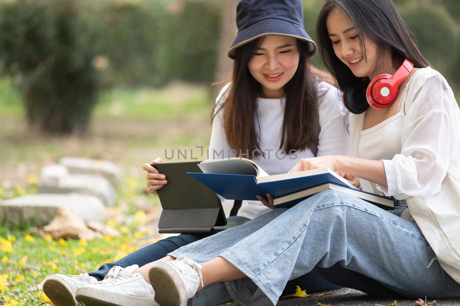 Two happy students sitting and talking each other in a campus at the park