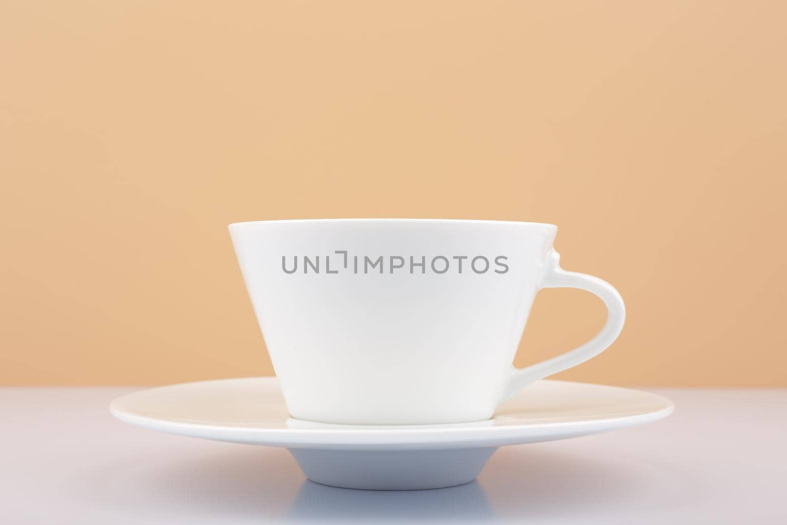 Selective focus, close up of white porcelain coffee or tea cup on white table against beige background. Concept of hot drinks and kitchenware