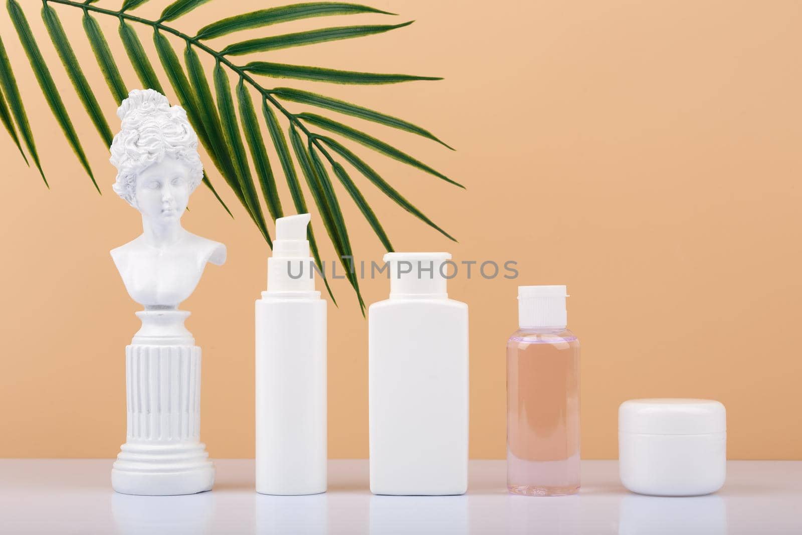 Set of skin care products with gypsum figure of a woman on white table against beige background with palm leaf. Face cream, lotion, tonic and under eye gel. Products for daily skin care
