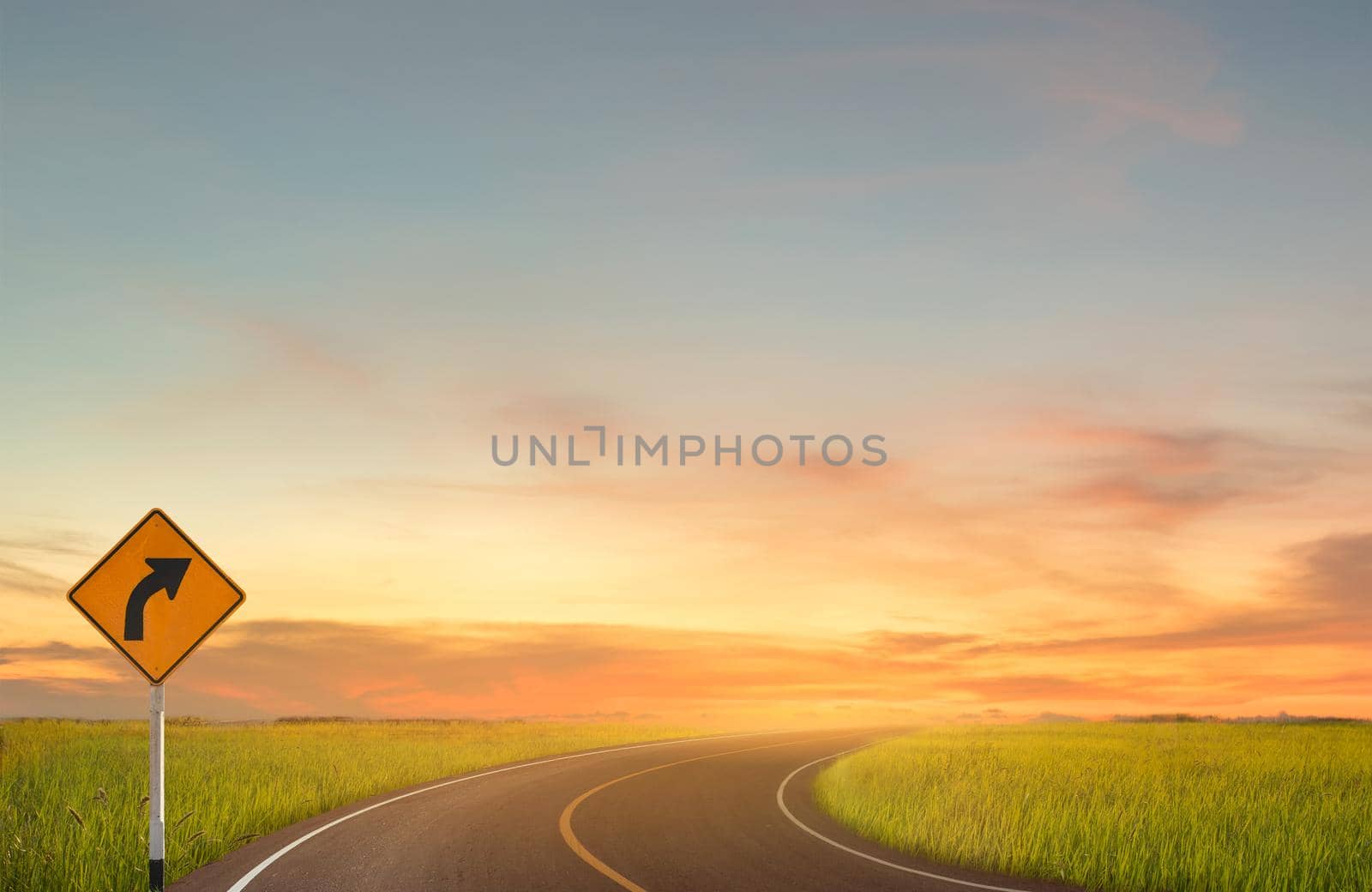 Sign curved road on the way at the natural sunset over field or meadow. Countryside Landscape Under Scenic Colorful Sky At Sunset. Nature Concept.