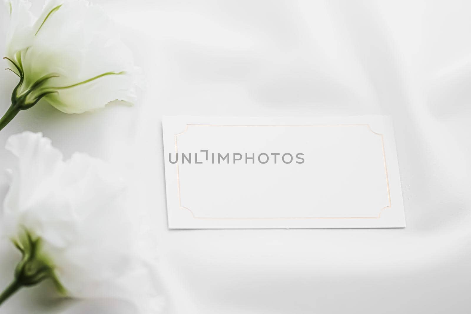 Wedding invitation or gift card and white rose flowers on silk fabric as bridal flatlay background, blank paper and holiday branding, flat lay design concept