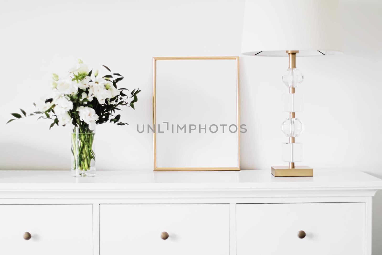 Golden vertical frame and bouquet of fresh flowers on white furniture, luxury home decor and design for mockup creation by Anneleven