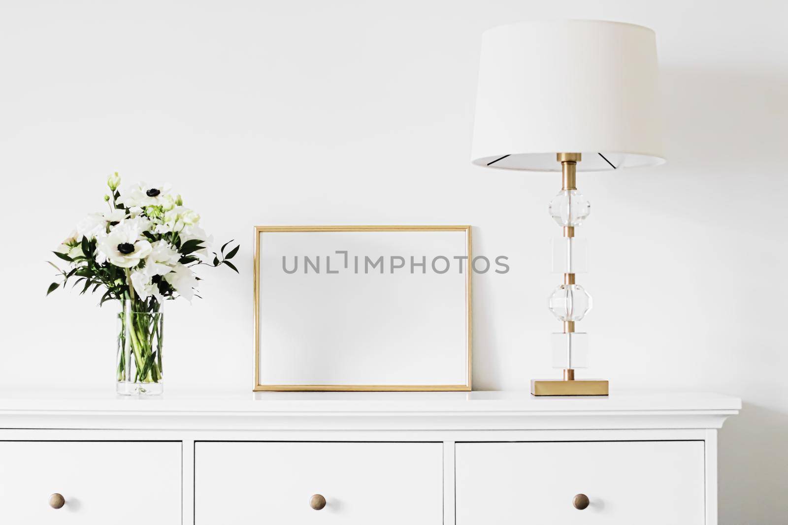 Golden horizontal frame and bouquet of fresh flowers on white furniture, luxury home decor and design for mockup creation by Anneleven