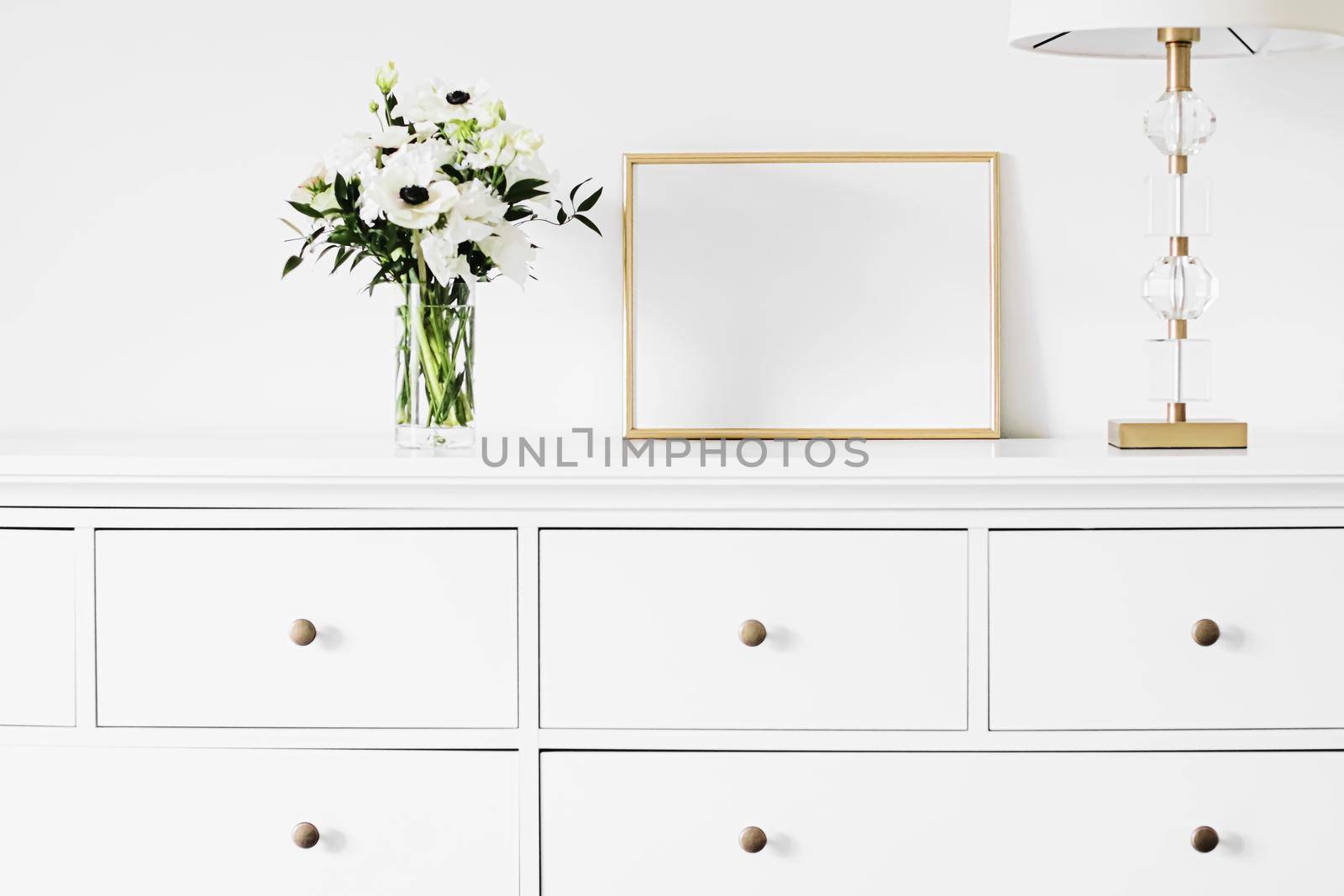 Golden horizontal frame and bouquet of fresh flowers on white furniture, luxury home decor and design for mockup creation by Anneleven