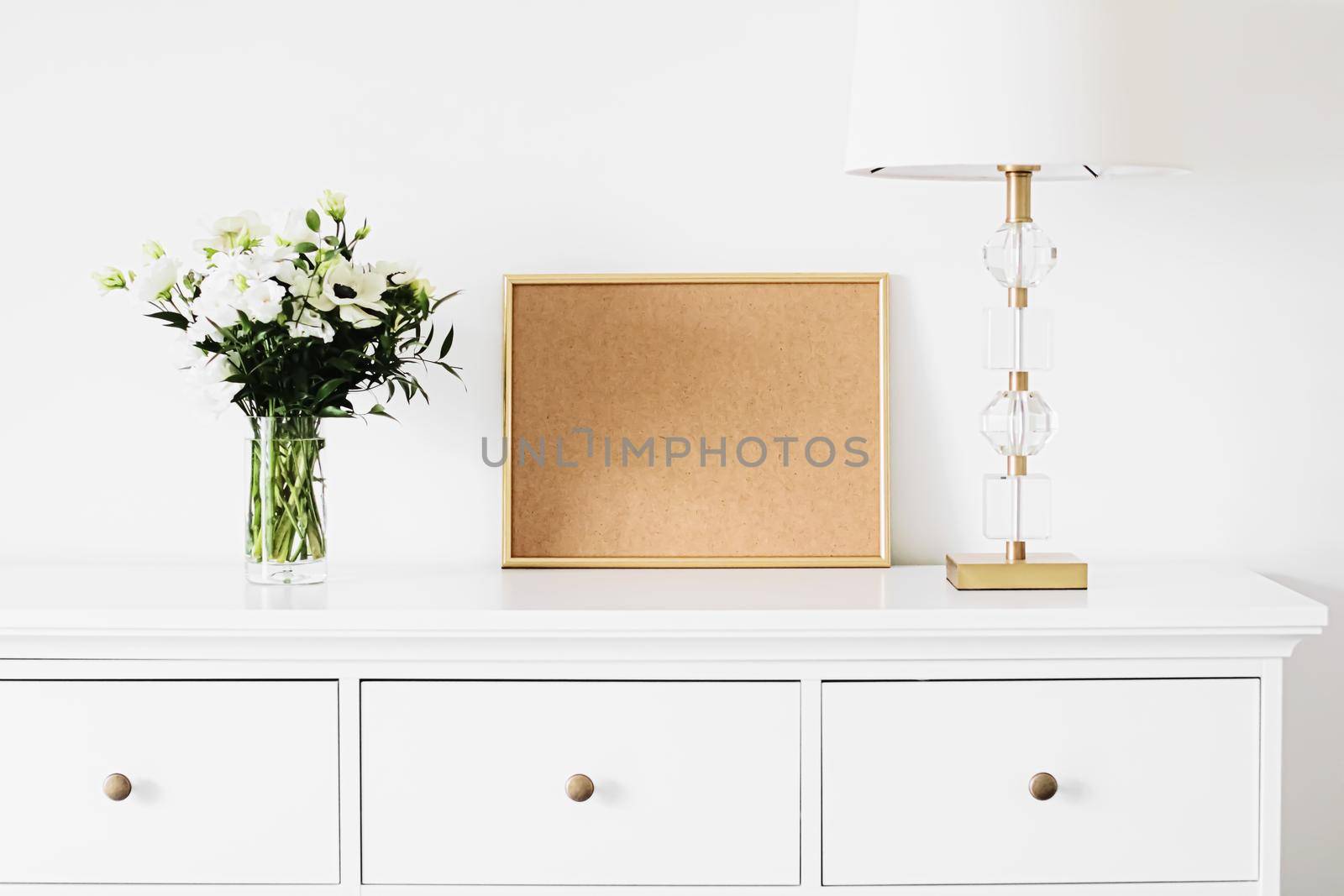 Golden horizontal frame and bouquet of fresh flowers on white furniture, luxury home decor and design for mockup creation by Anneleven