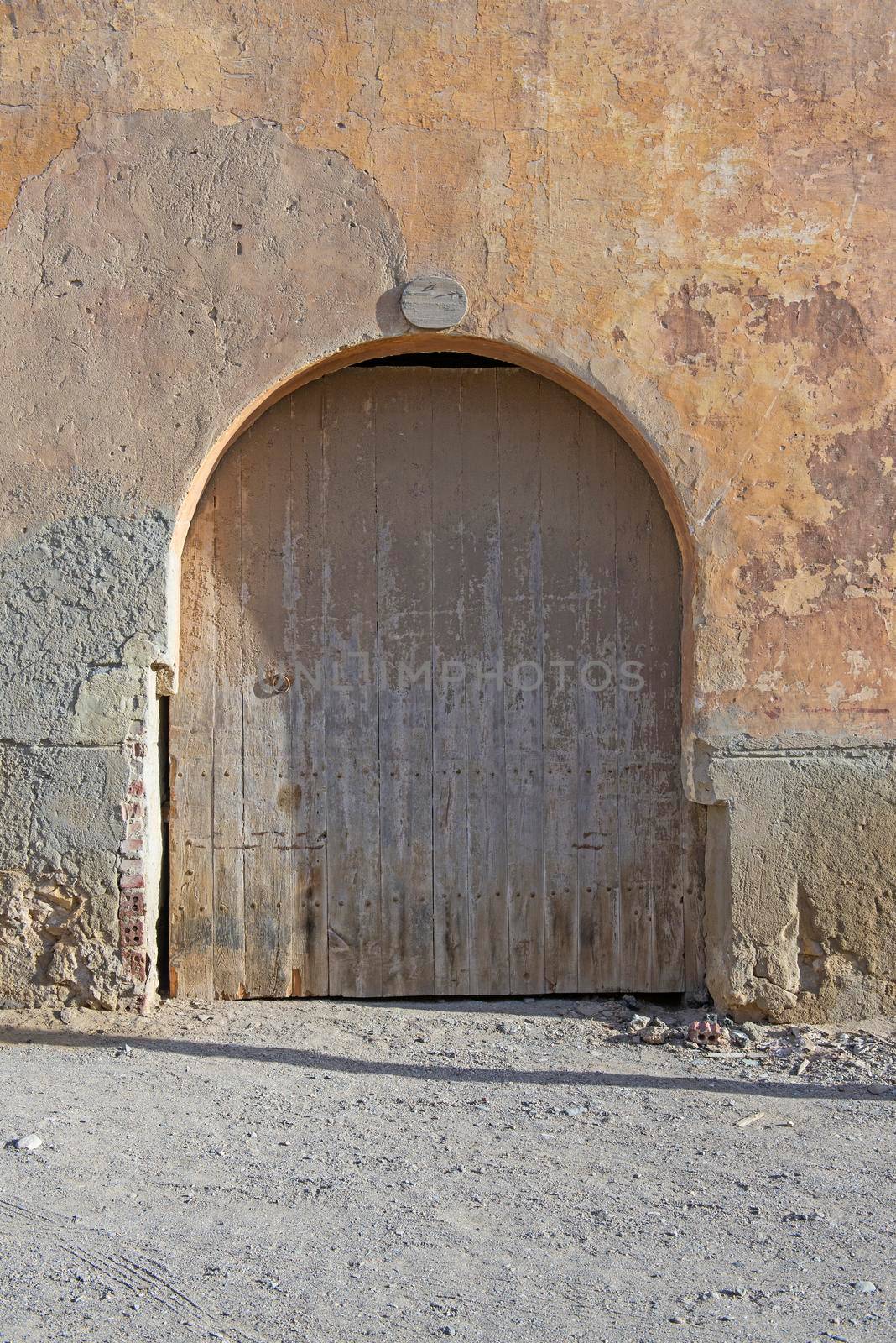 Old rustic wooden arched door in wall of abandoned traditional egyptian house