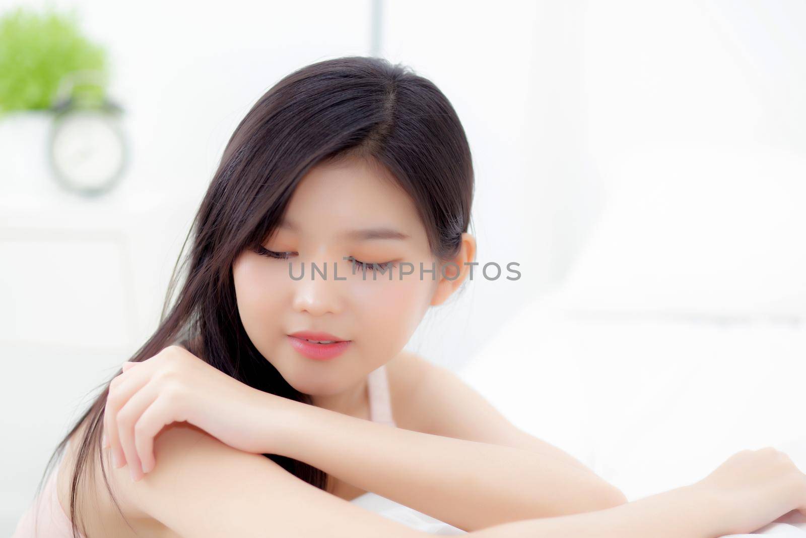 Beautiful young asian woman applying moisturizer with makeup of cosmetic, girl hand touch shoulder cream and lotion attractive, beauty perfect with wellness in the bedroom with skin care concept.