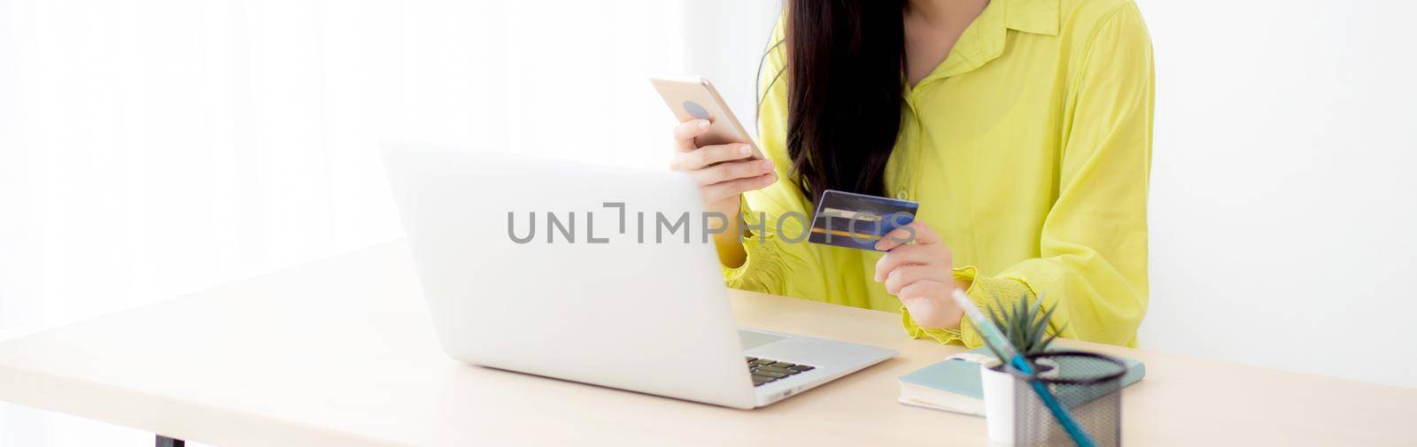 Young asian business woman using smart phone and holding credit card while online shopping and payment online with laptop computer on desk at home, female holding debit card, communication concept. by nnudoo