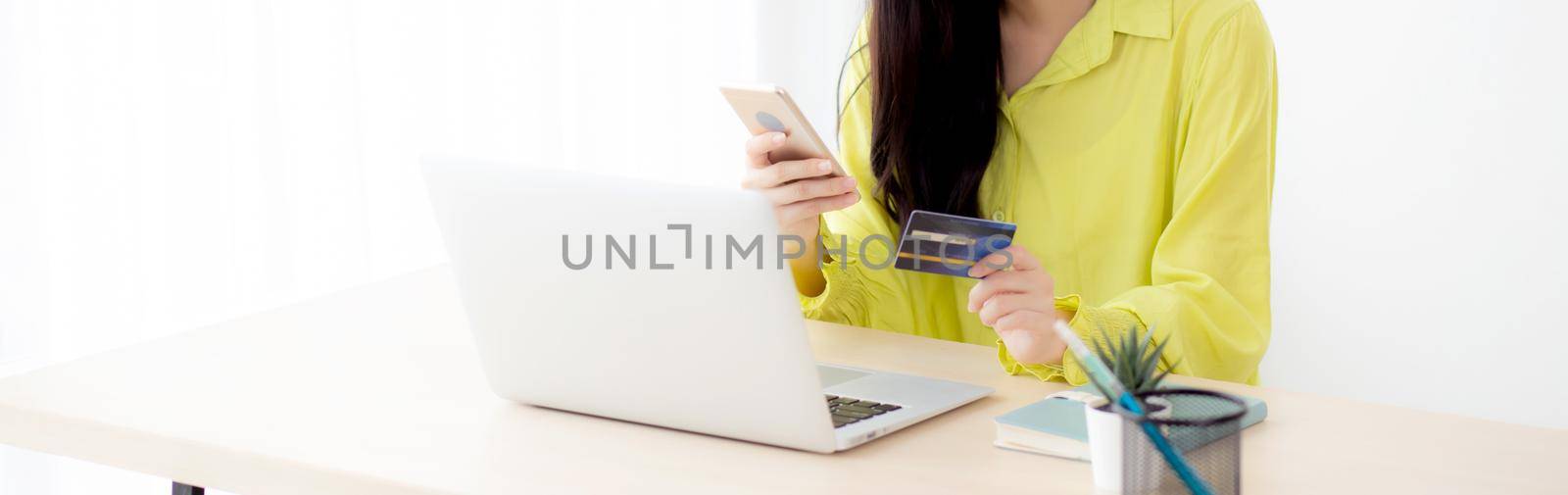 Young asian business woman using smart phone and holding credit card while online shopping and payment online with laptop computer on desk at home, female holding debit card, communication concept.