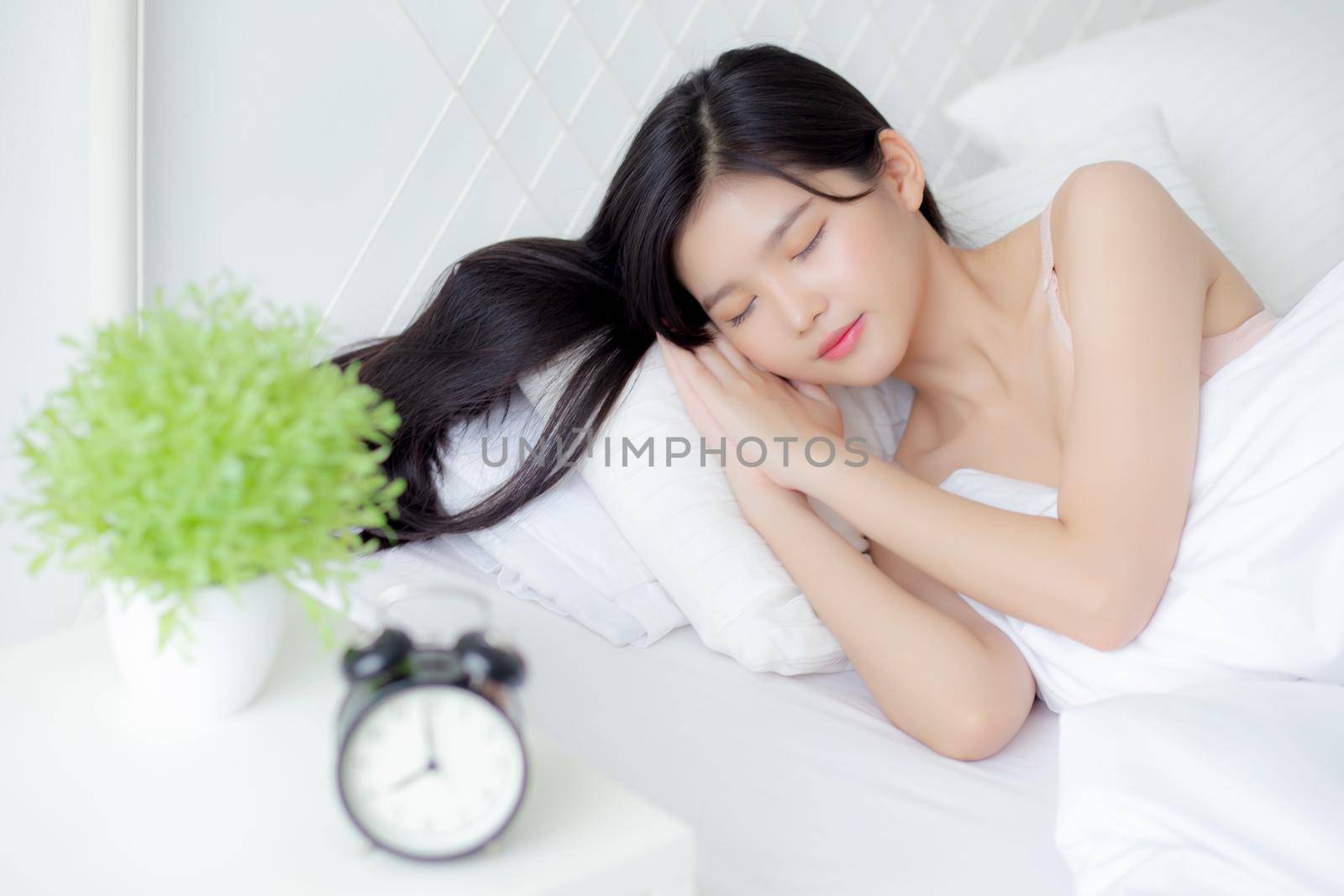 beautiful young asian woman sleep with relax on the bed with alarm clock in the morning, girl sleep with cozy and comfort after tired in the bedchamber, oversleep with time late, lifestyle concept.