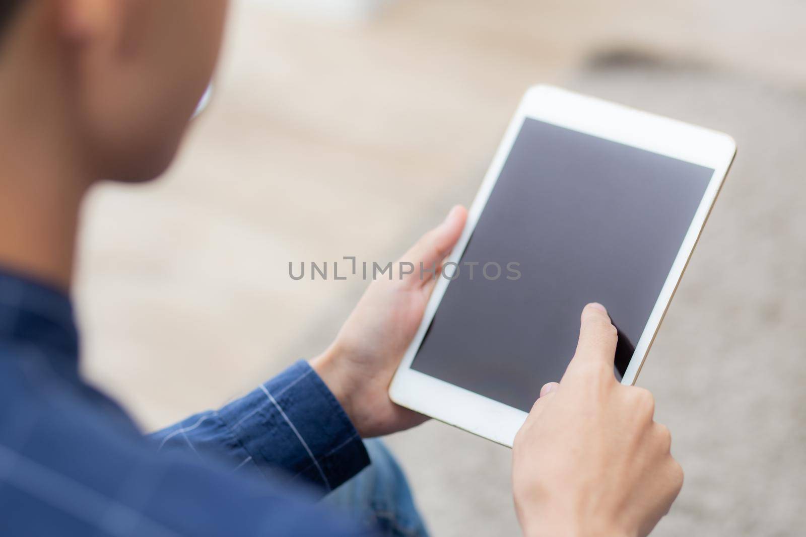 Closeup young asian man sitting and using mockup of tablet computer with display blank screen on sofa at home, male holding digital tablet watch entertainment at living room, communication concept.