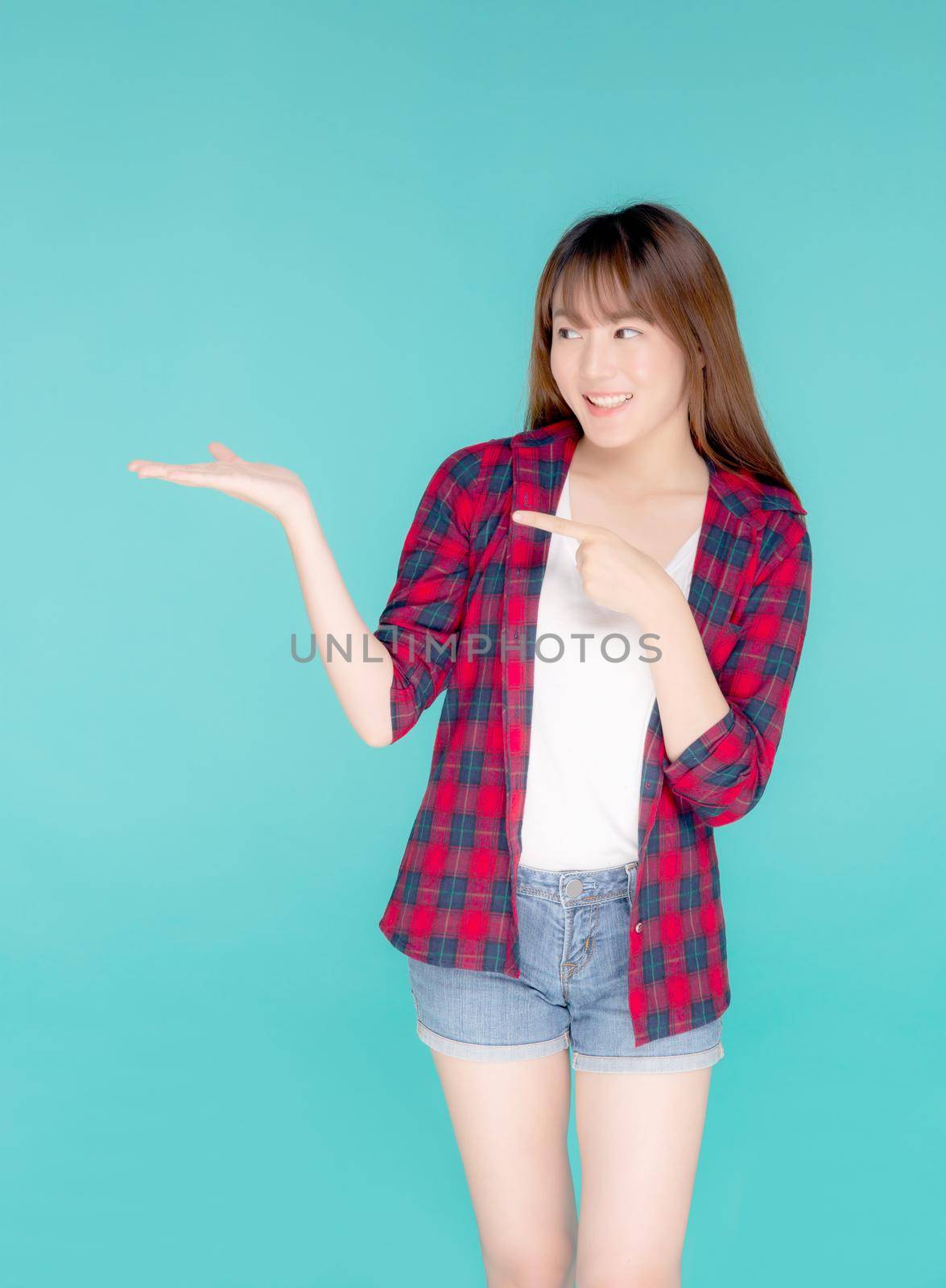 Beautiful portrait young asian woman smiling gesture presenting something and pointing summer holiday isolated blue background, asia girl excited and cheerful with journey, travel concept. by nnudoo